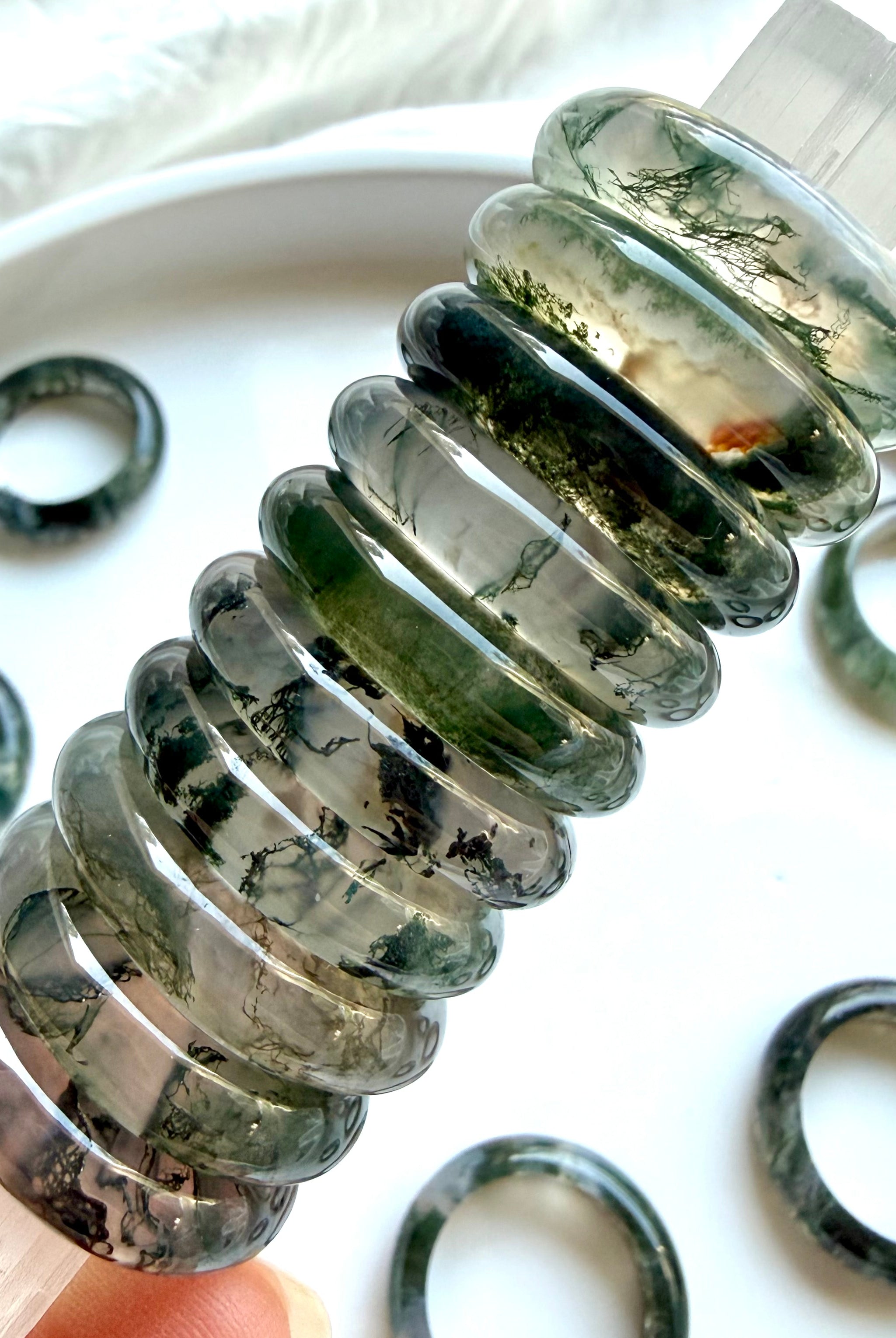 stacked moss agate band rings on selenite wand highlighting translucence and natural dendritic inclusions, crystal rings for grounding, clarity, and heart chakra balance