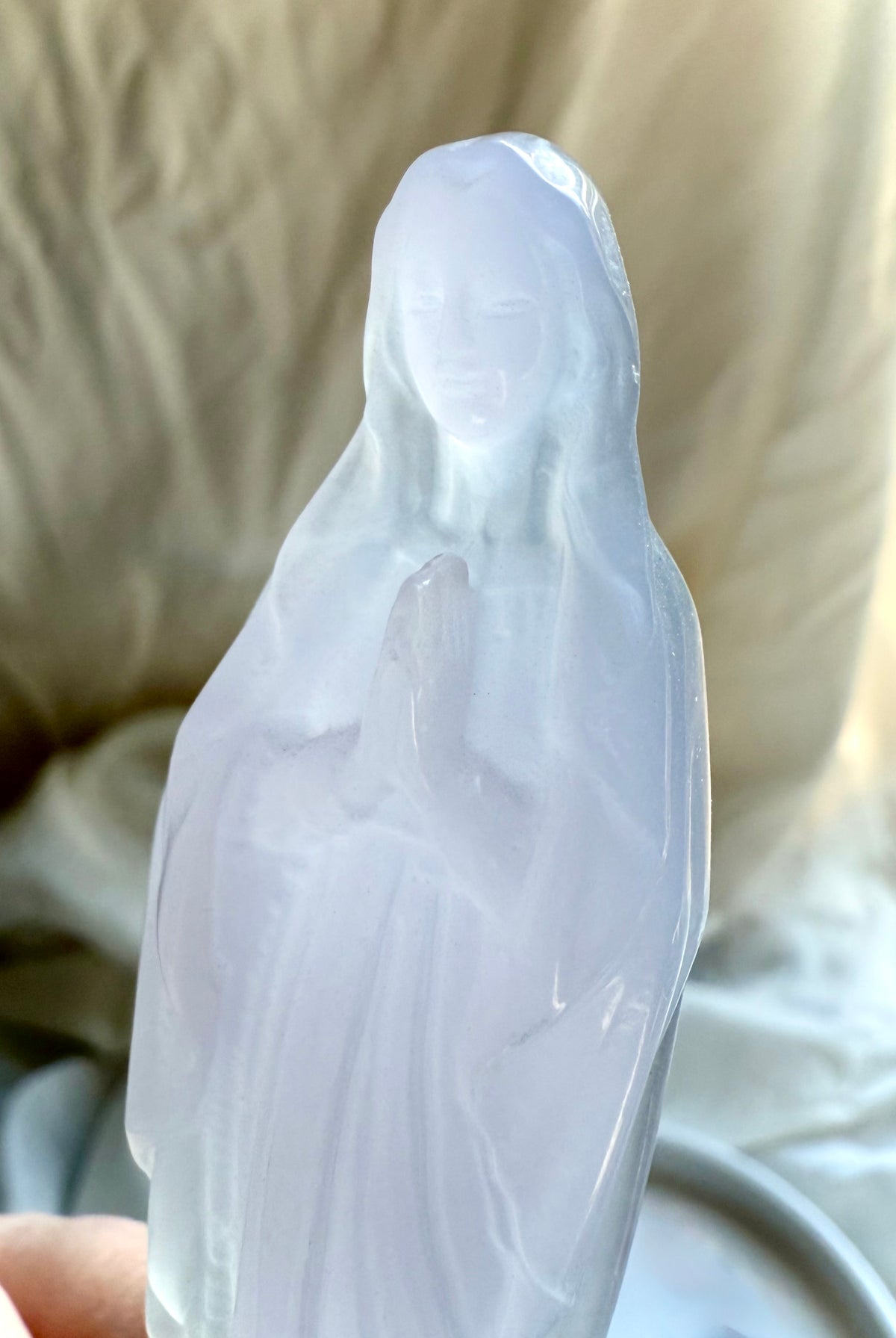 Mother Mary crystal carving held in hand, showing the soft translucent lavender and green coloring of Yttrium Fluorite