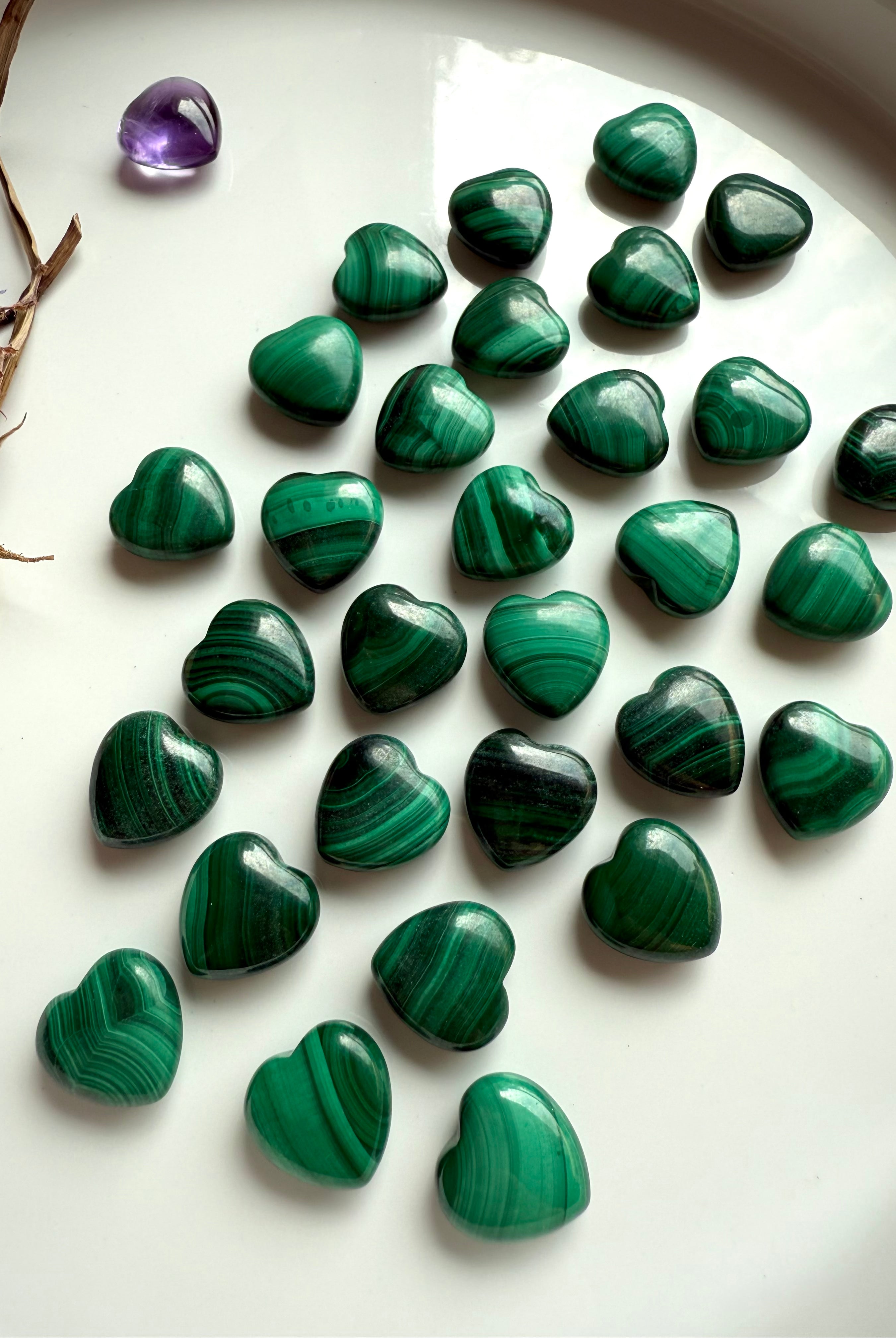 Glossy green Malachite crystal hearts displayed on a white dish with dried flowers & a mini amethyst heart.