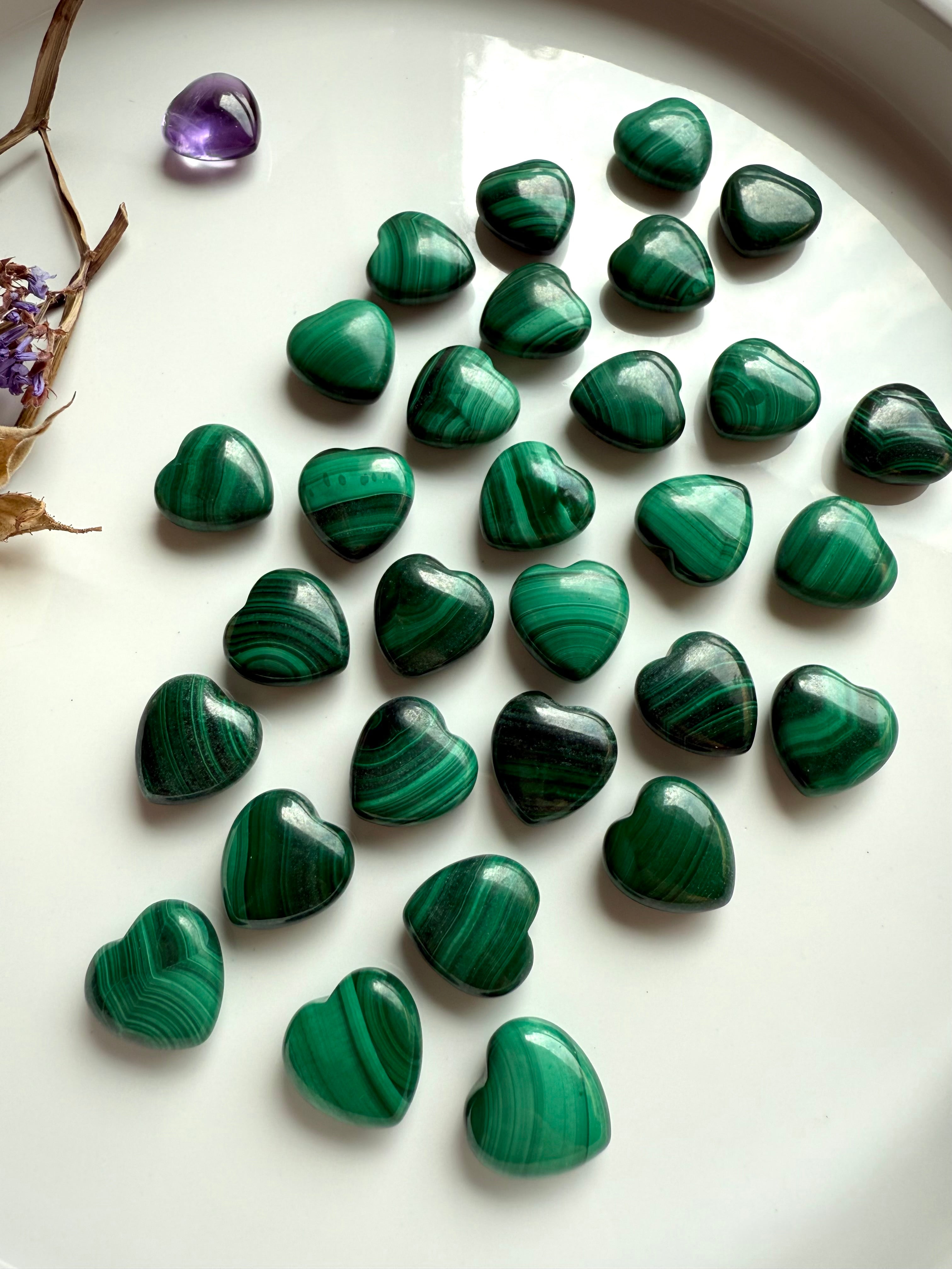 Glossy green Malachite crystal hearts displayed on a white dish with dried flowers & a mini amethyst heart.