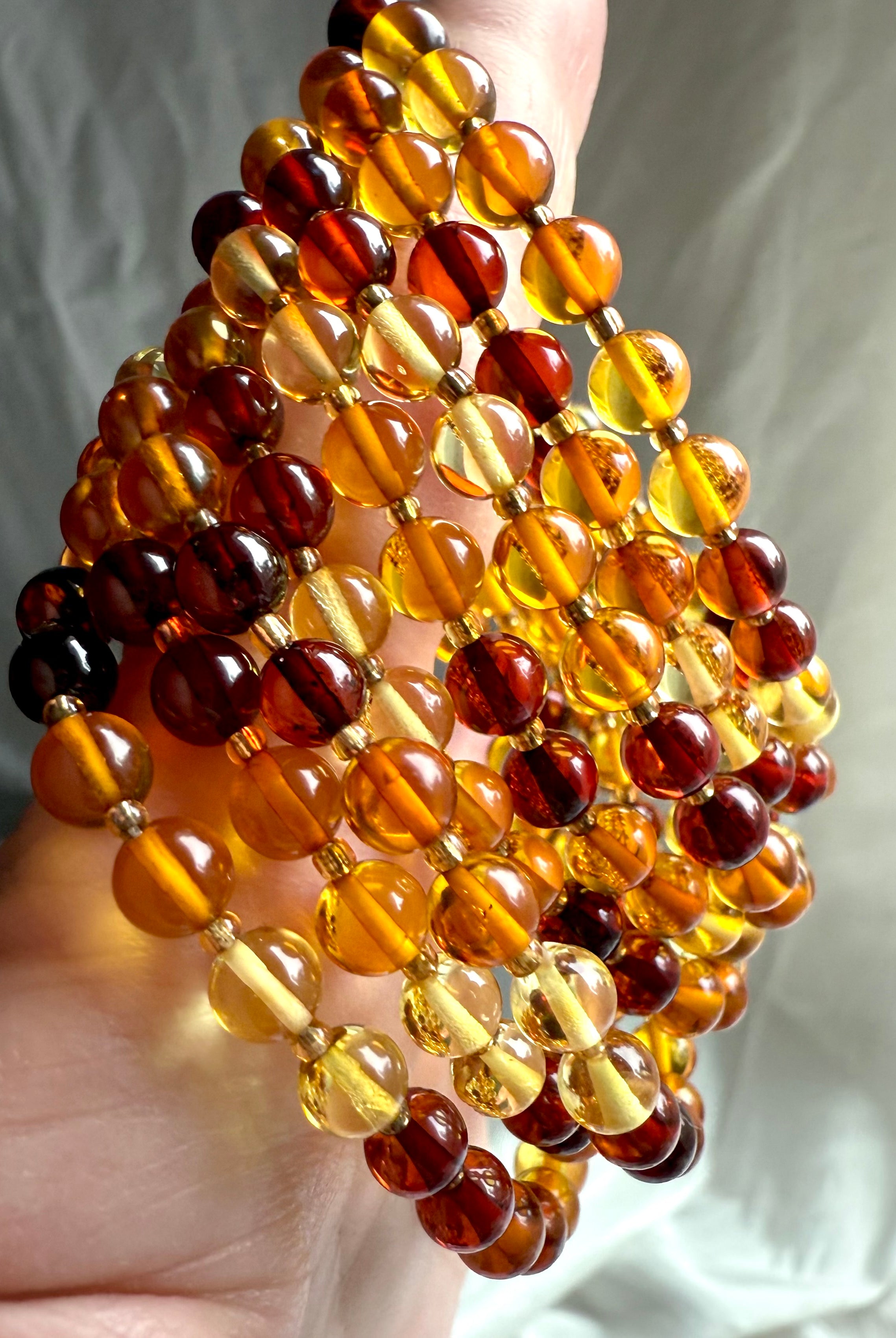 Amber bracelets draped in hand with vibrant color variation – energizing crystal jewelry for confidence + life force