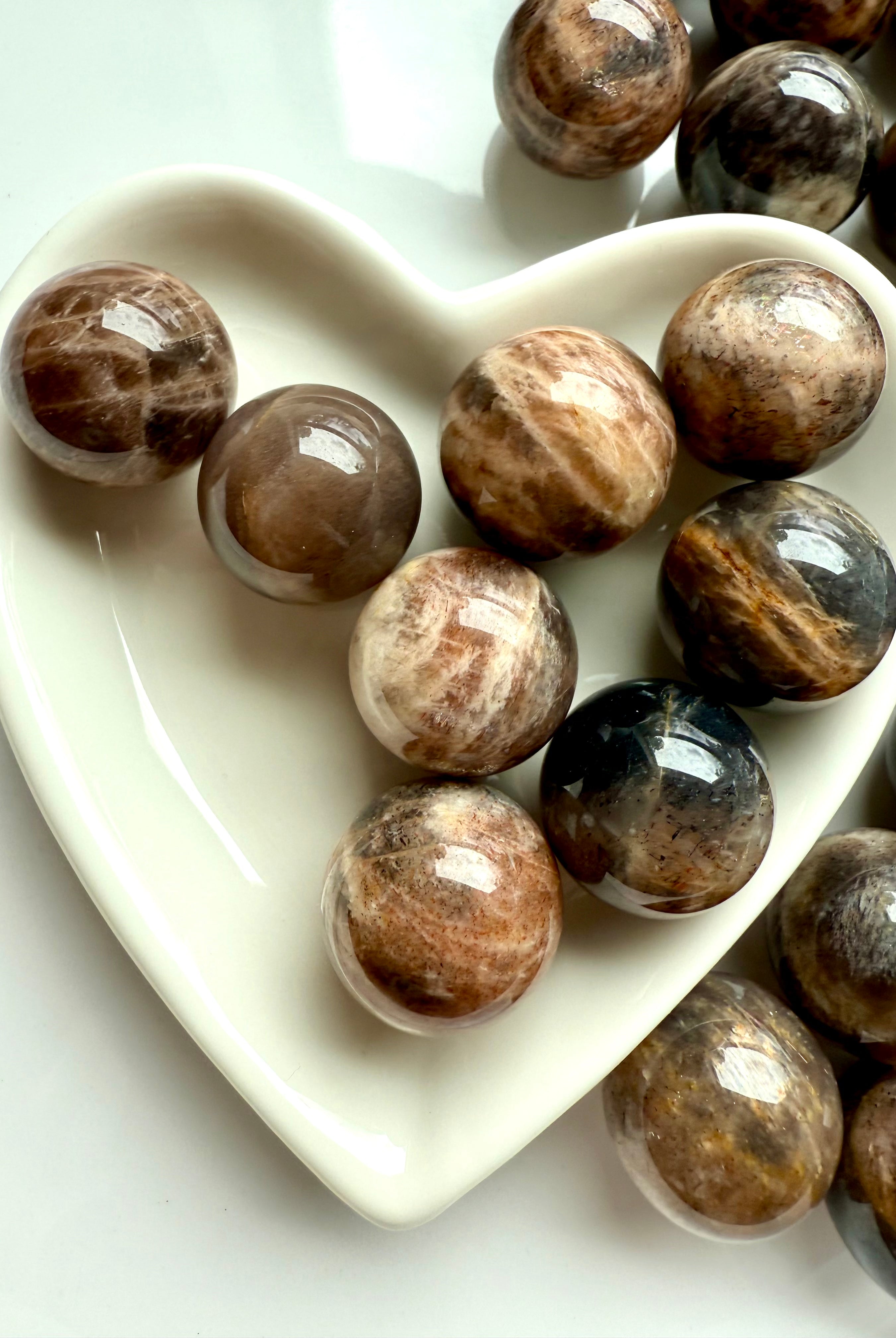 Closeup of Mini Black Moonstone spheres with Sunstone shimmer displayed in a white heart-shaped bowl