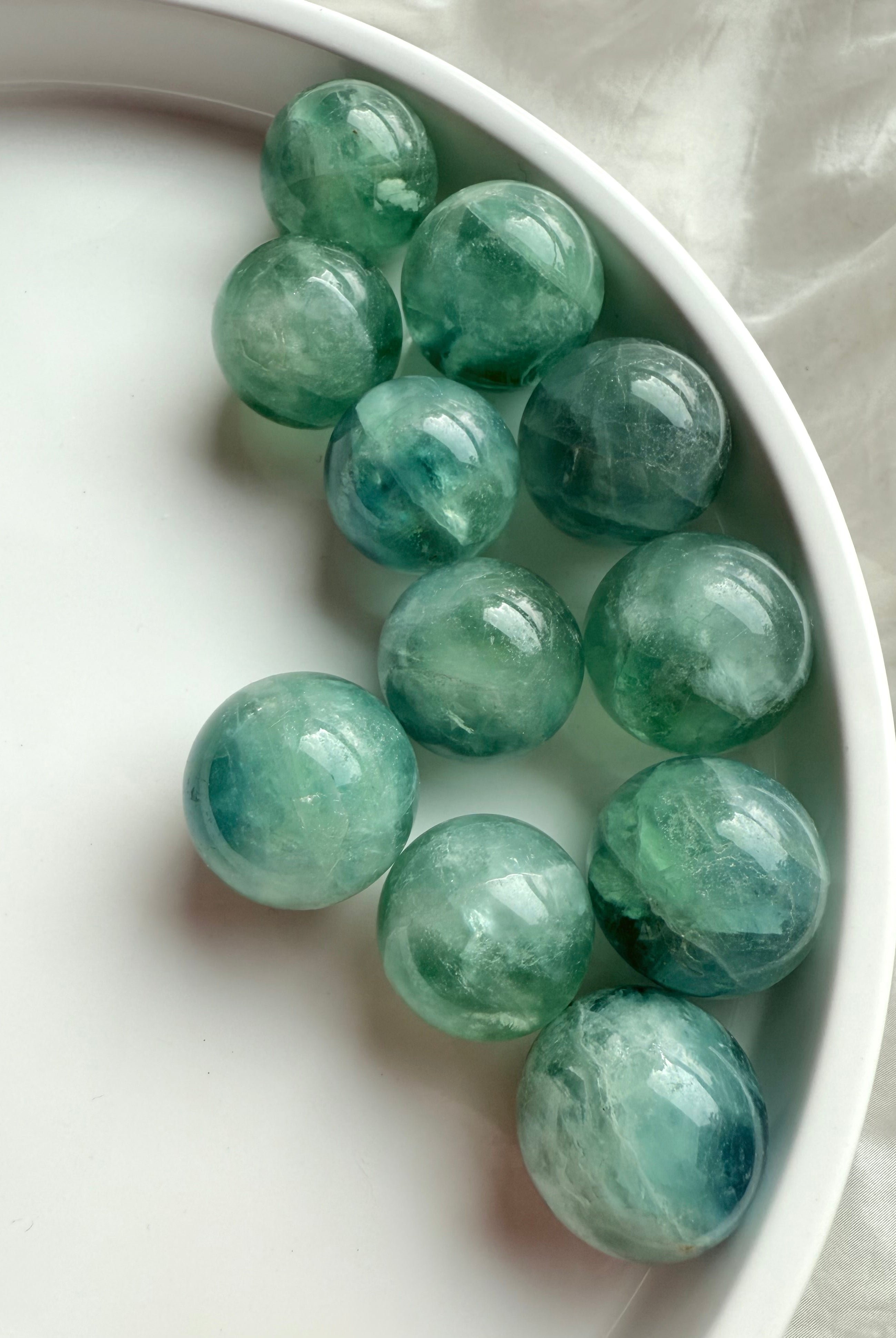 Teal Fluorite spheres with aqua green glow displayed on a white tray, mini crystal balls for clarity and throat chakra healing.