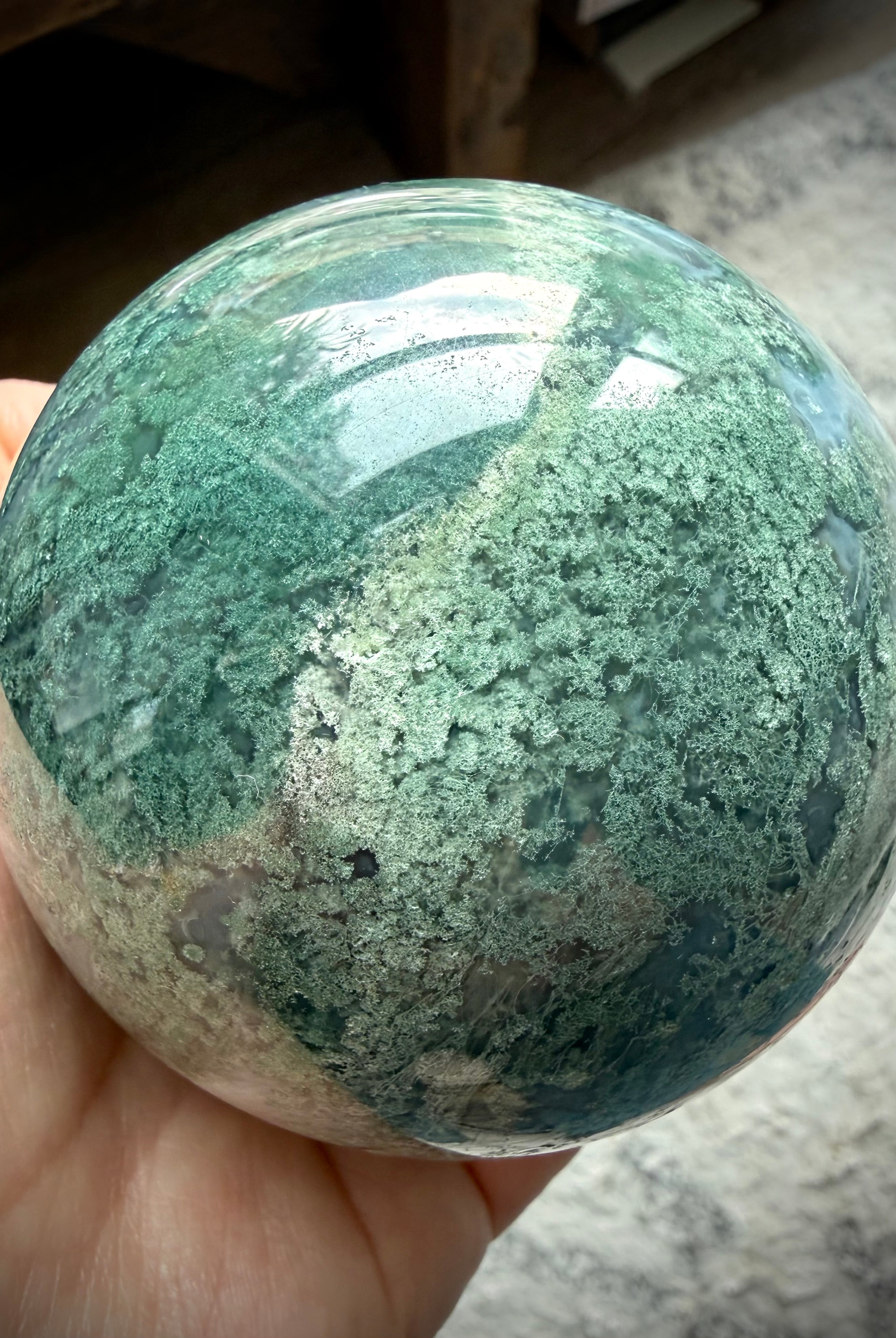 Polished Moss Agate sphere showing translucent areas, crystal formations, and forest-like inclusions