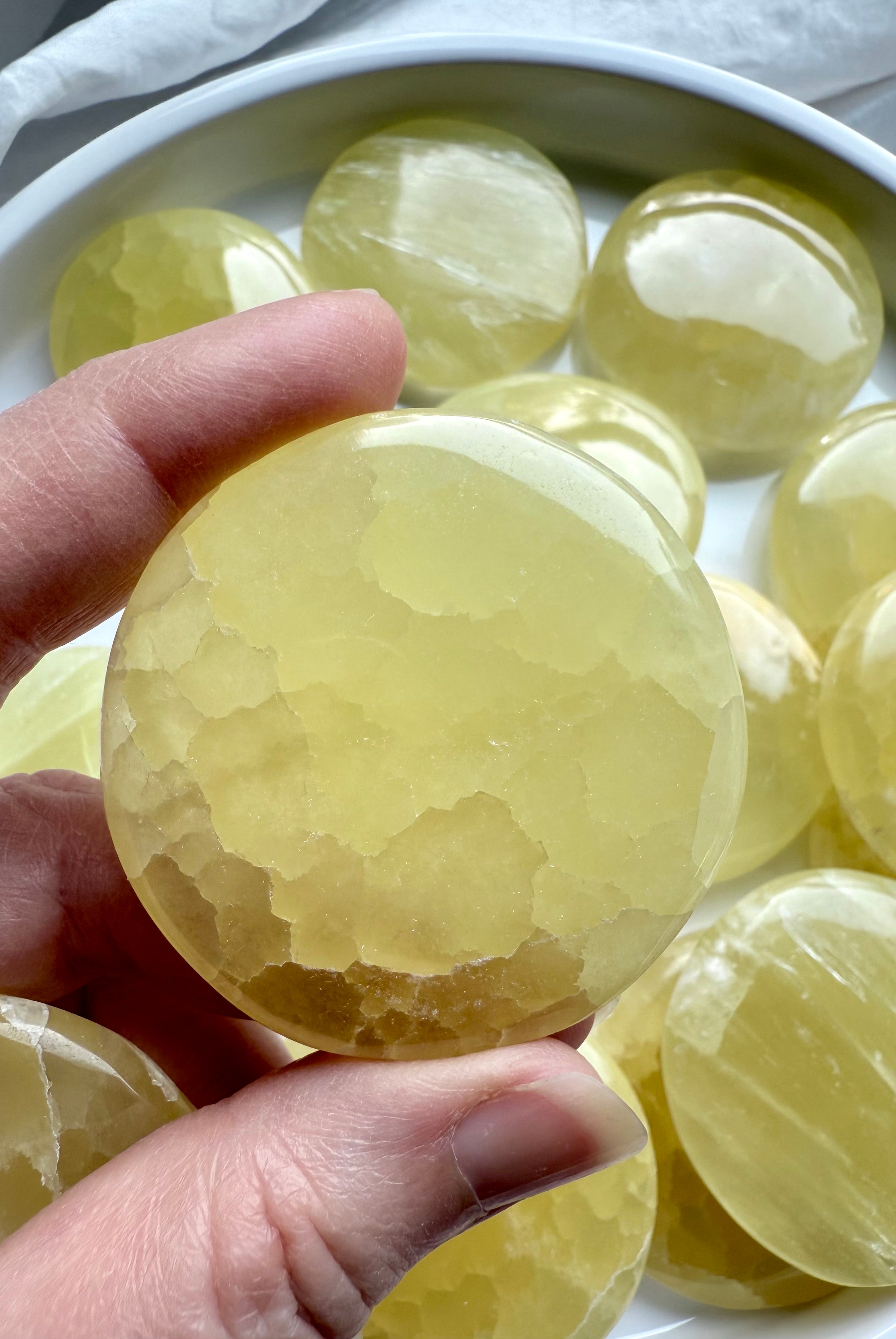 Polished lemon calcite meditation stone held above a white bowl filled with yellow crystals