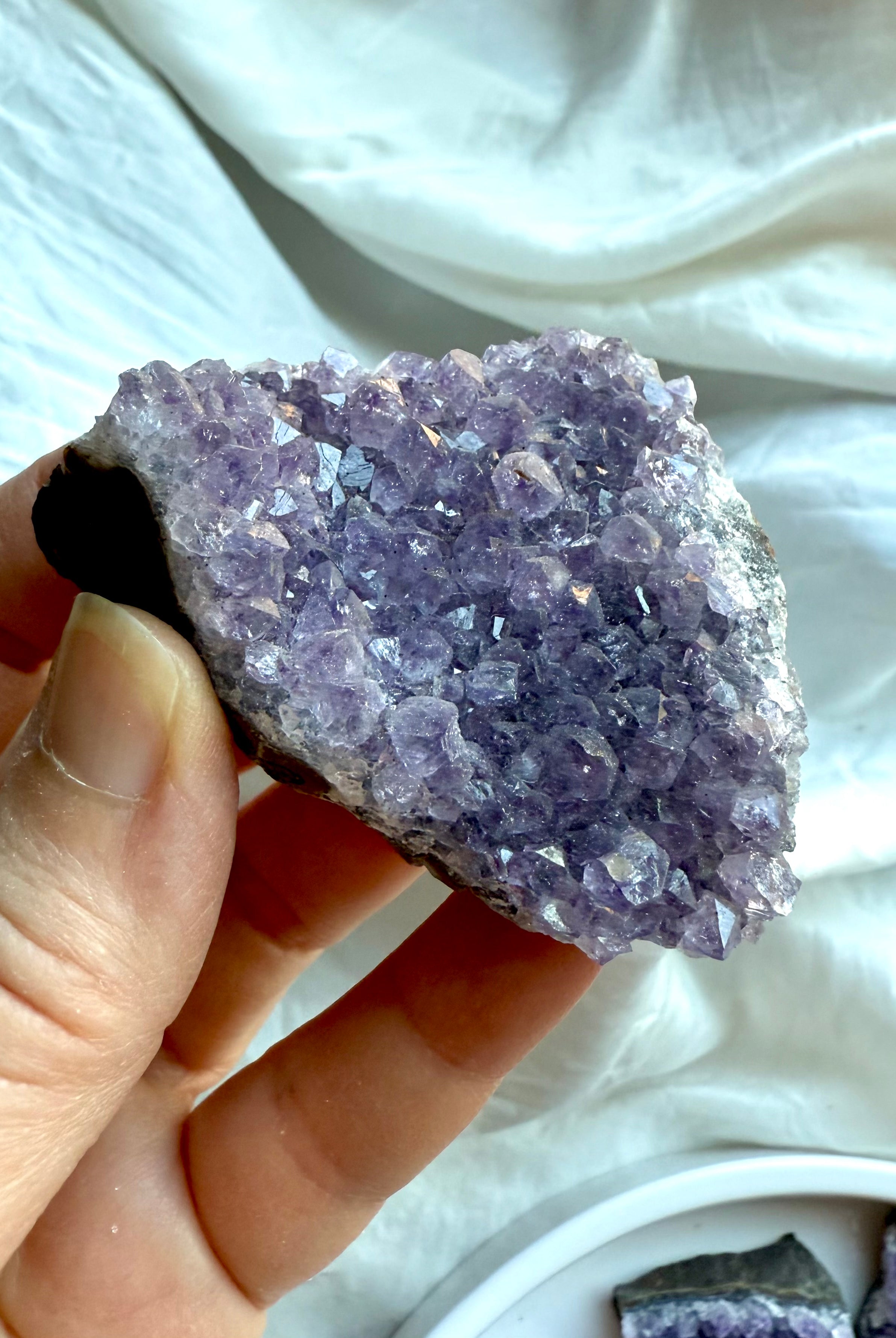 Closeup of natural amethyst geode cluster held in hand over white silk. Third Eye Chakra crystal for intuition.