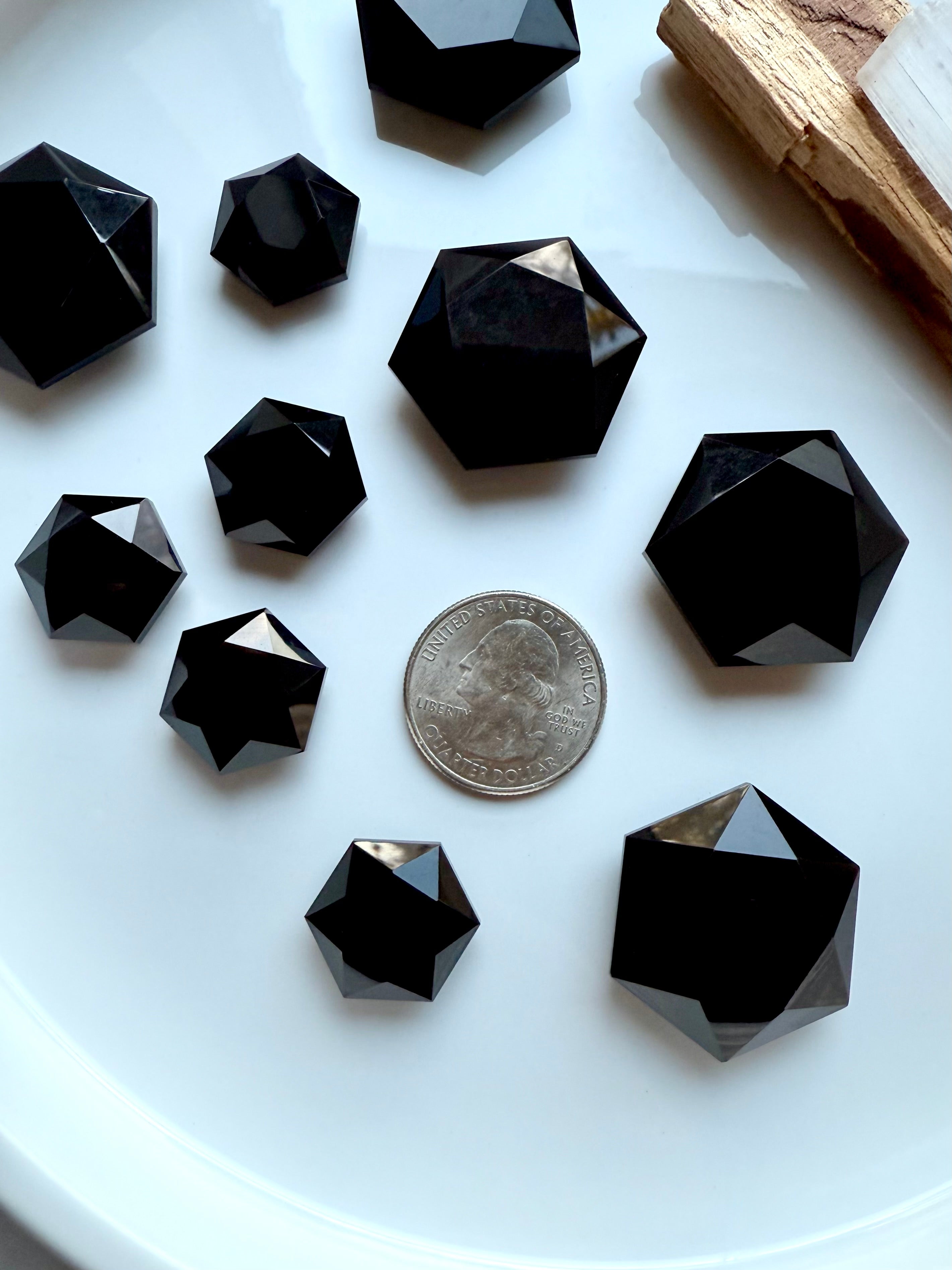 Faceted Black Obsidian hexagon crystal shown in two sizes beside a quarter for size reference, glossy black sacred geometry carving