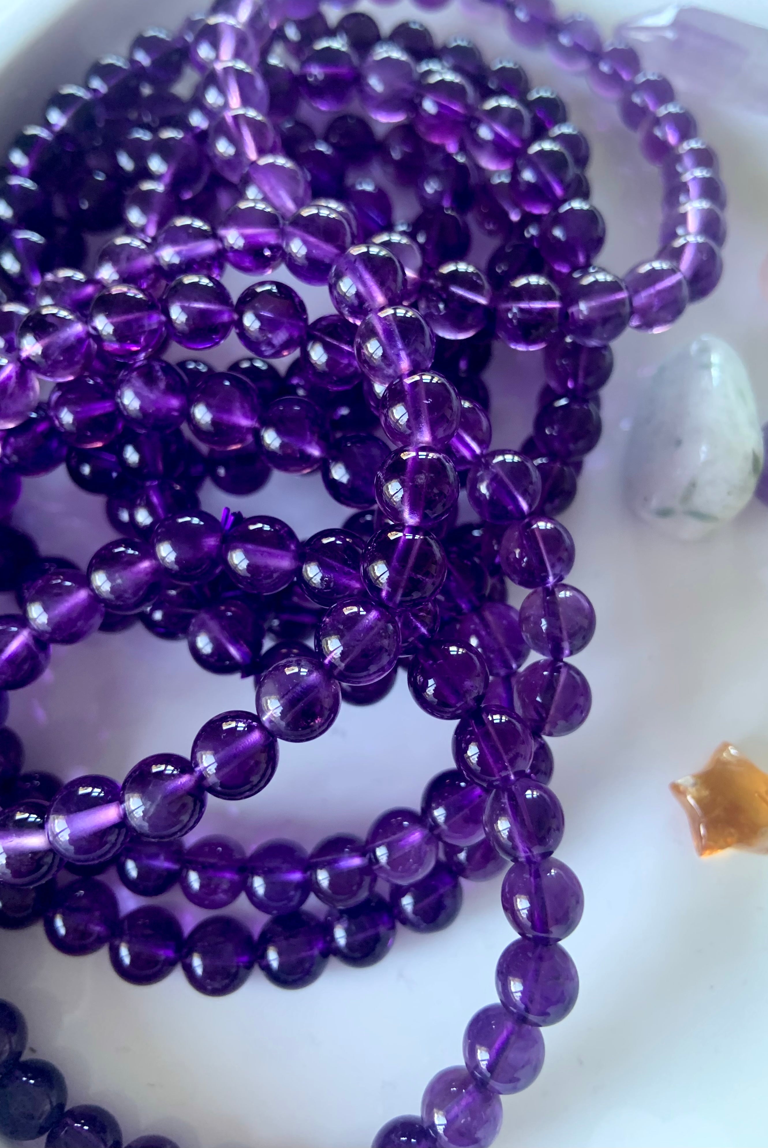 An array of high quality amethyst bracelets on a white plate with other mini crystals in the background