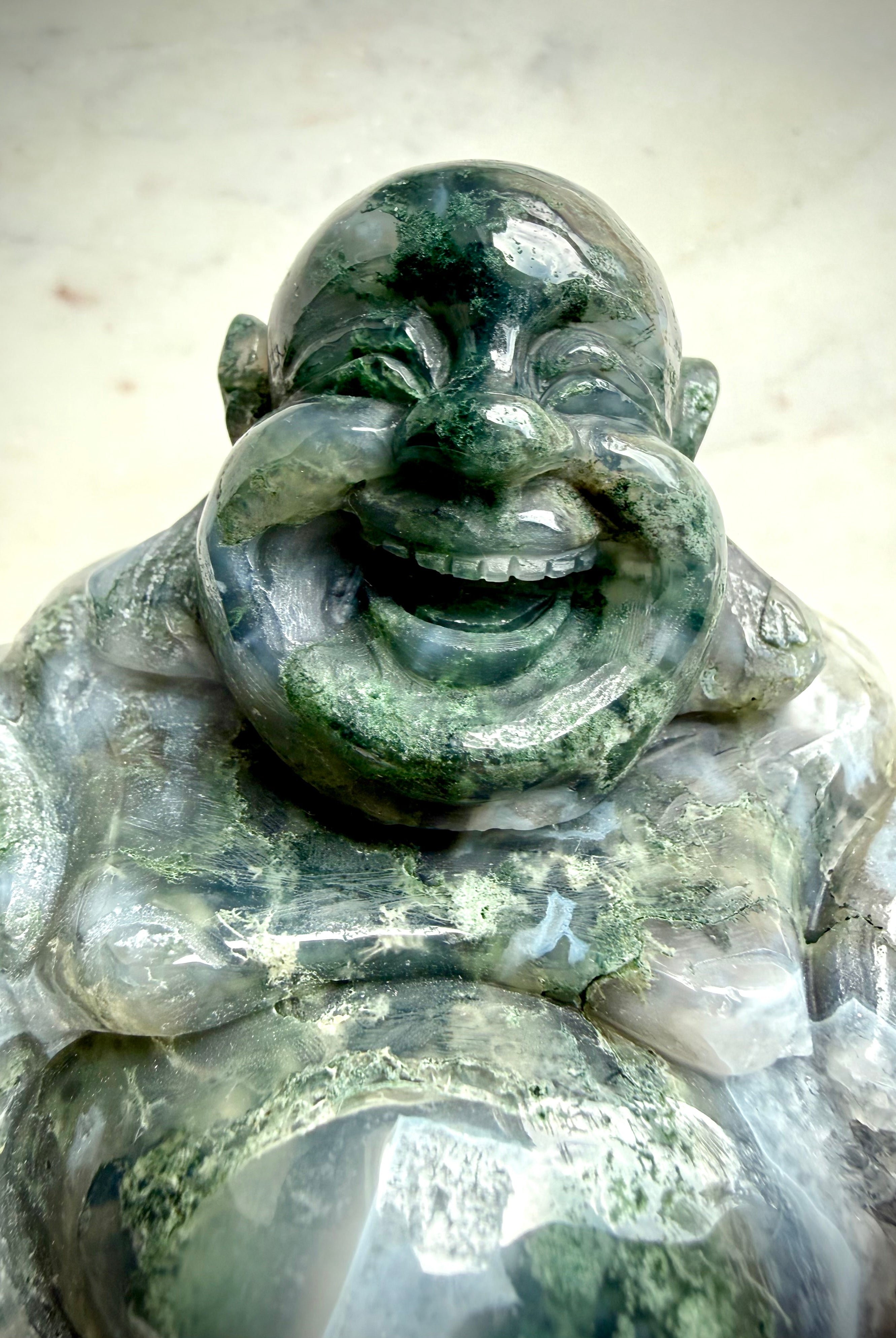 Closeup view of a Large Moss Agate Laughing Buddha statue highlighting detailed hand carving