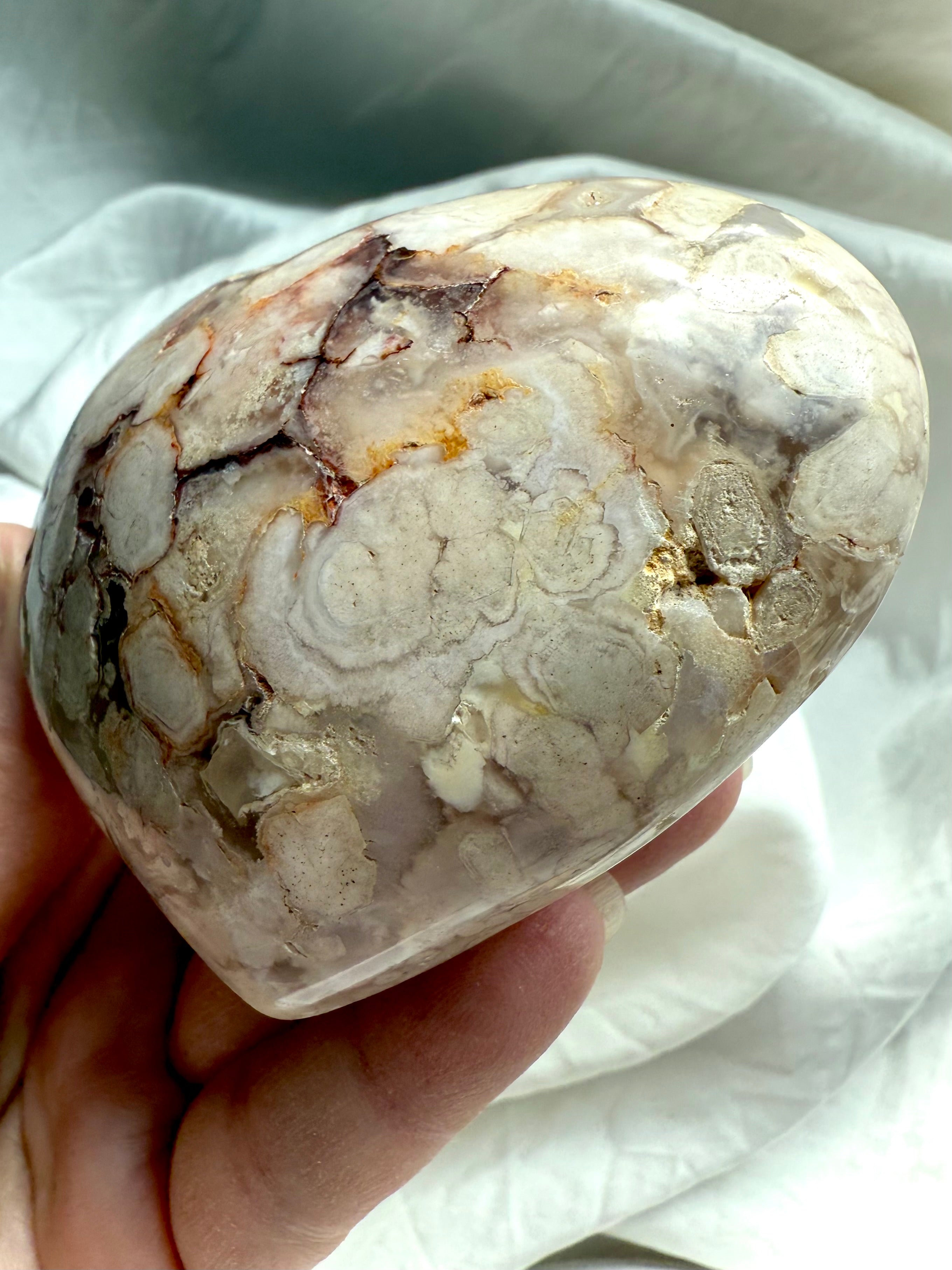 Angled view of a Flower Agate heart held in hand, revealing layered chalcedony blooms โ soothing stone for emotional clarity, nurturing energy, and inner growth.