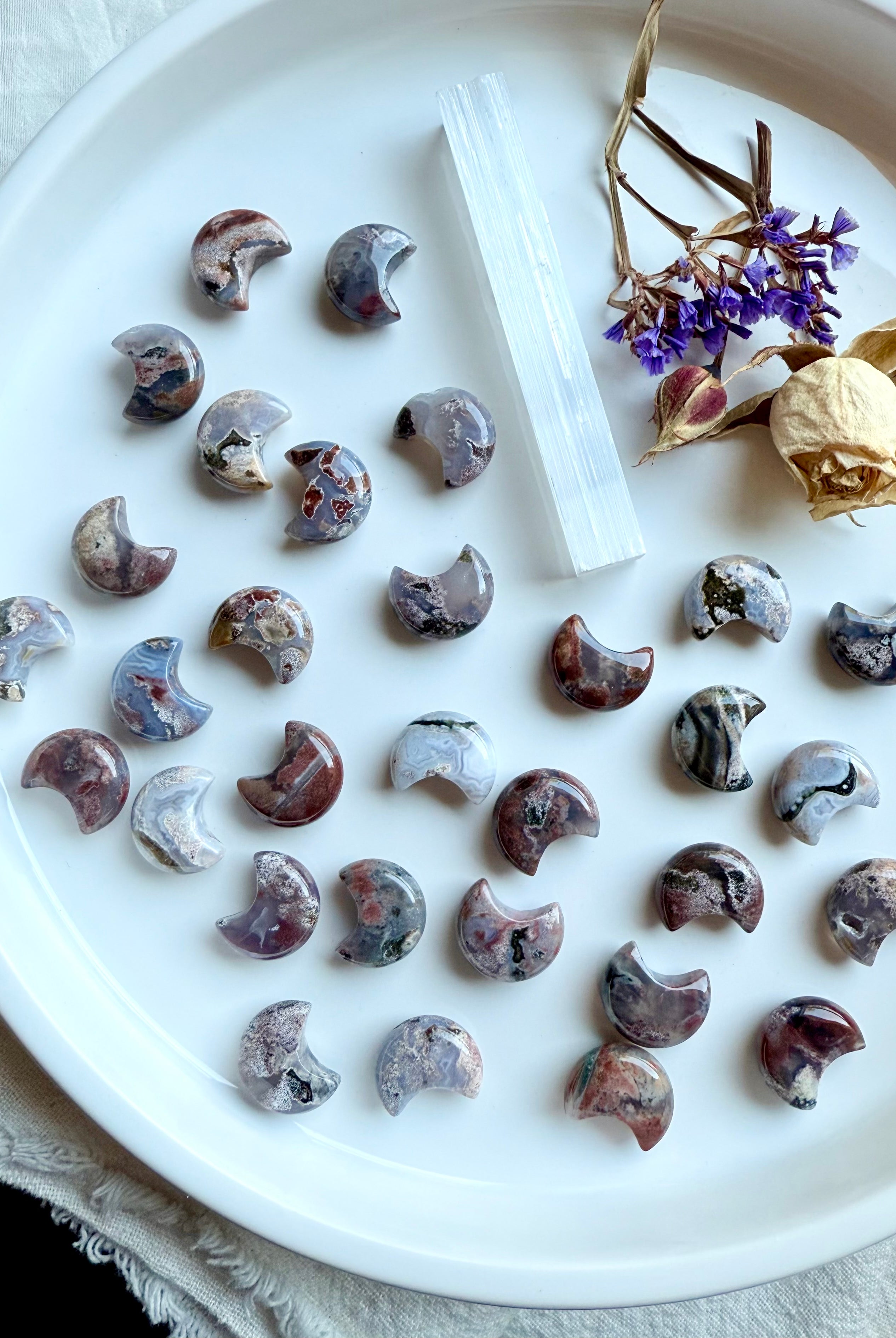 Ocean Jasper crescent moon carvings on white dish with selenite wand and dried flowers, celestial crystal carvings for altar décor and crystal grids