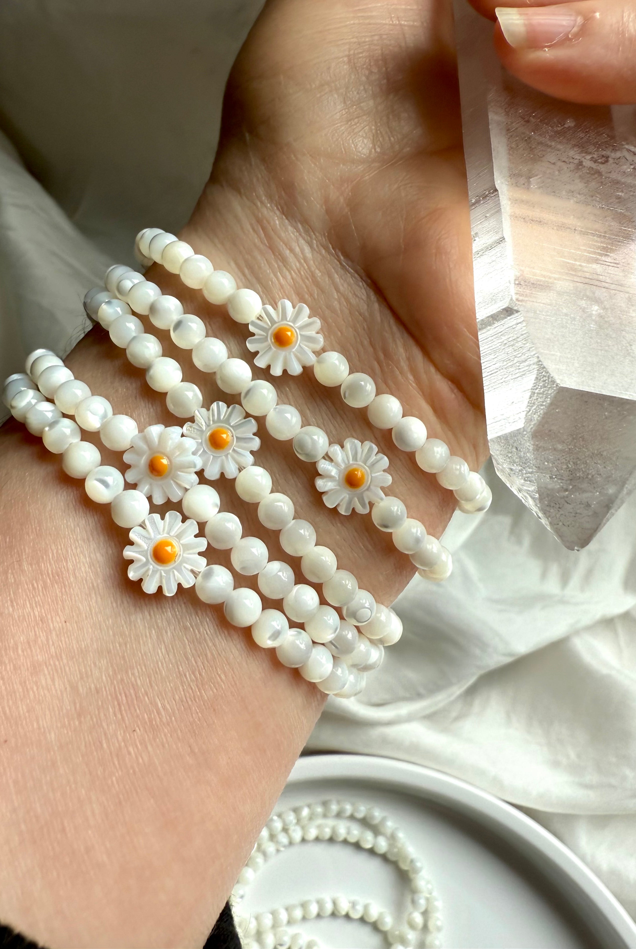 Mother of Pearl daisy bracelets on wrist with carved shell flowers and white iridescent beads, styled with Lemurian quartz crystal wand