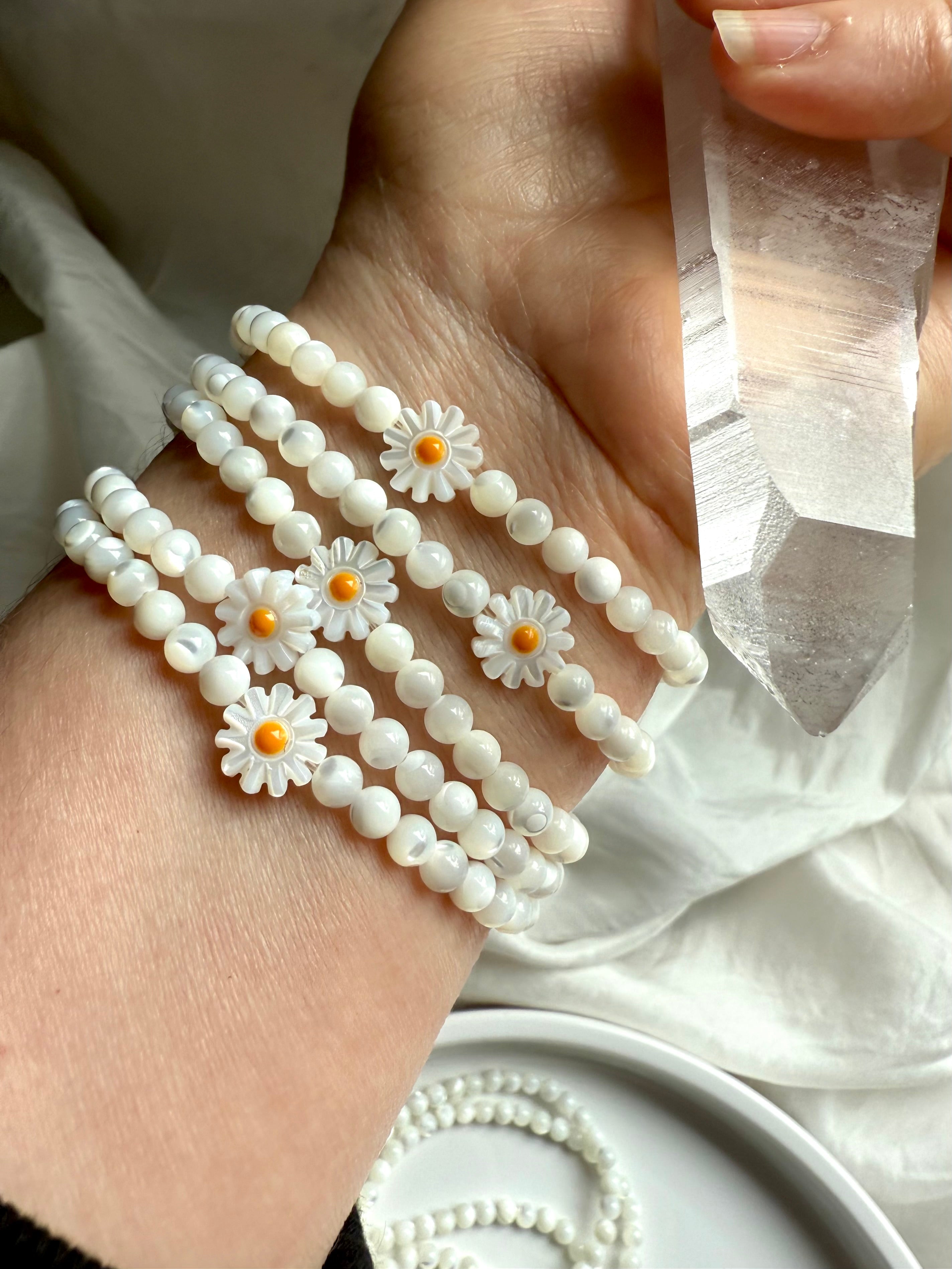 Mother of Pearl daisy bracelets on wrist with carved shell flowers and white iridescent beads, styled with Lemurian quartz crystal wand