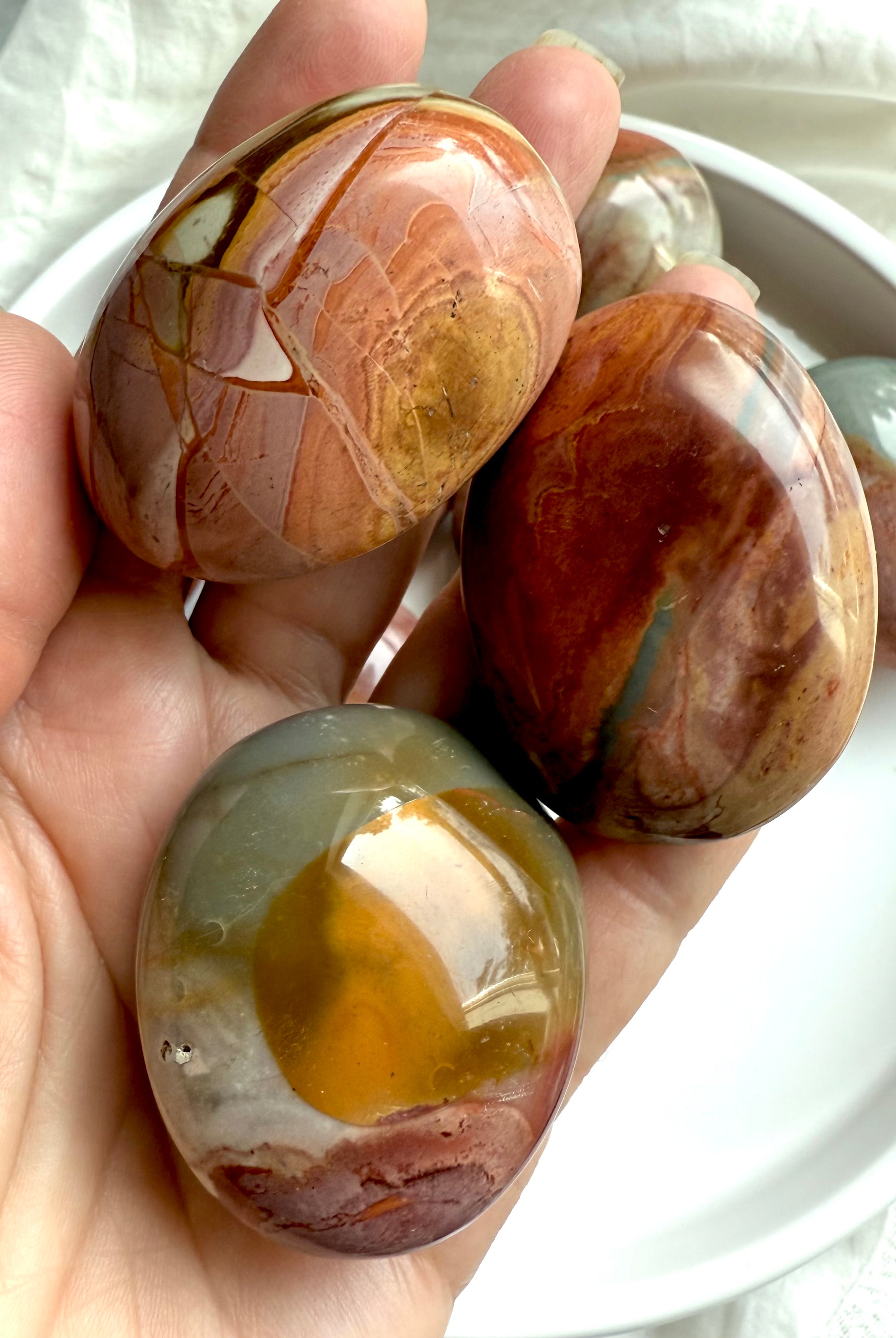 Polychrome Jasper palm stones in natural tones with swirling patterns shown on a hand.