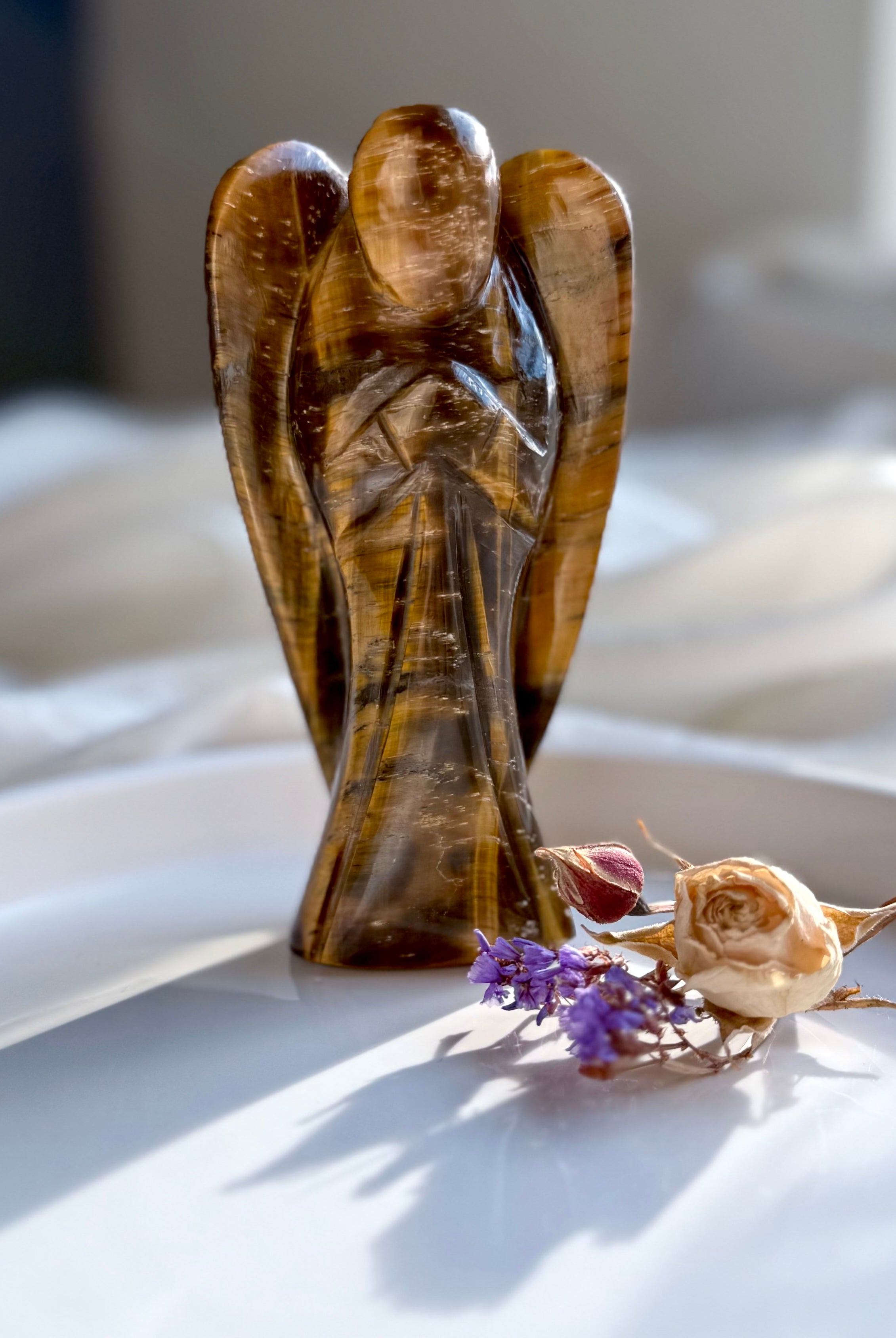 Hand-carved Tiger’s Eye angel standing upright with dried florals on a white ceramic tray