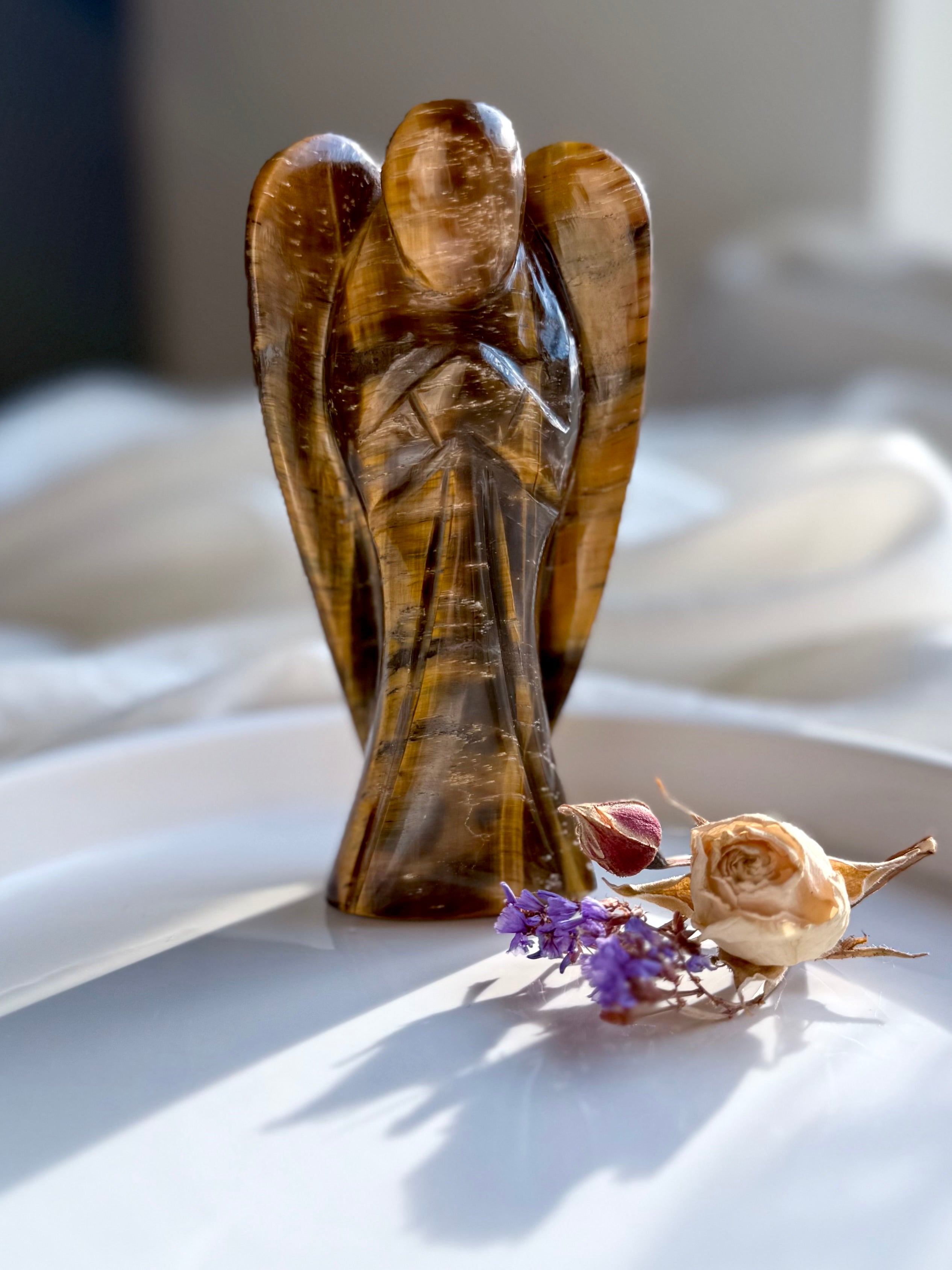 Hand-carved Tiger’s Eye angel standing upright with dried florals on a white ceramic tray