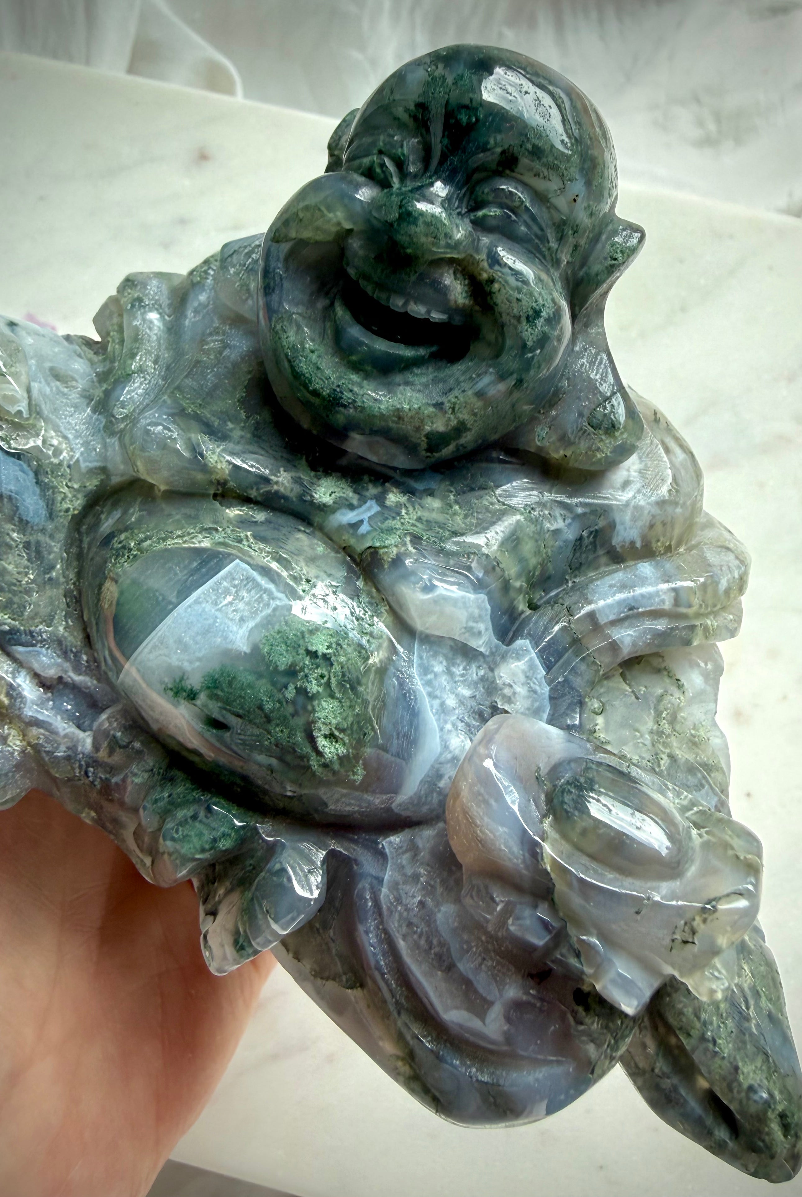 Large Moss Agate Laughing Buddha close-up highlighting scenic inclusions, natural translucence, and polished crystal detail