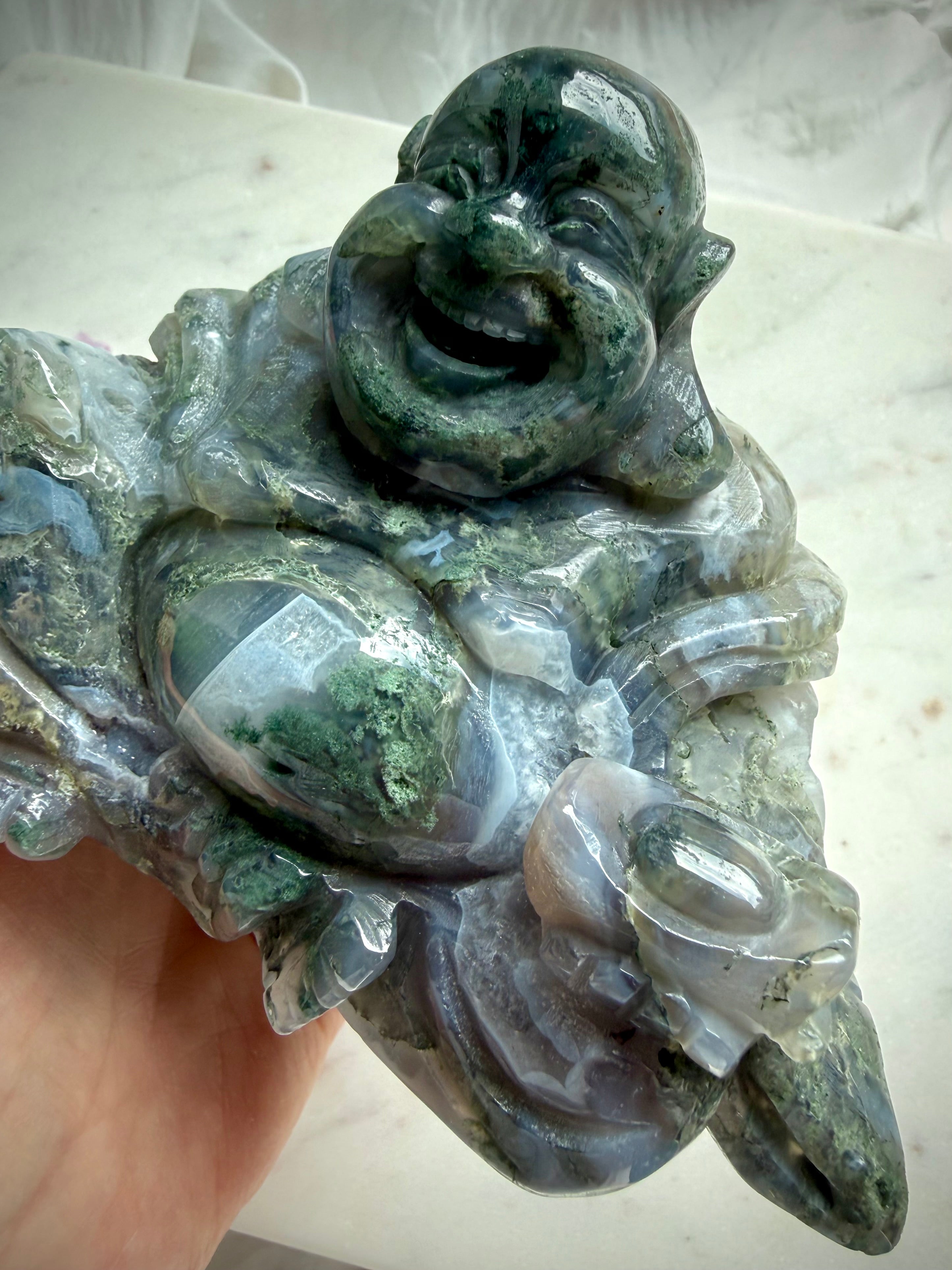 Large Moss Agate Laughing Buddha close-up highlighting scenic inclusions, natural translucence, and polished crystal detail