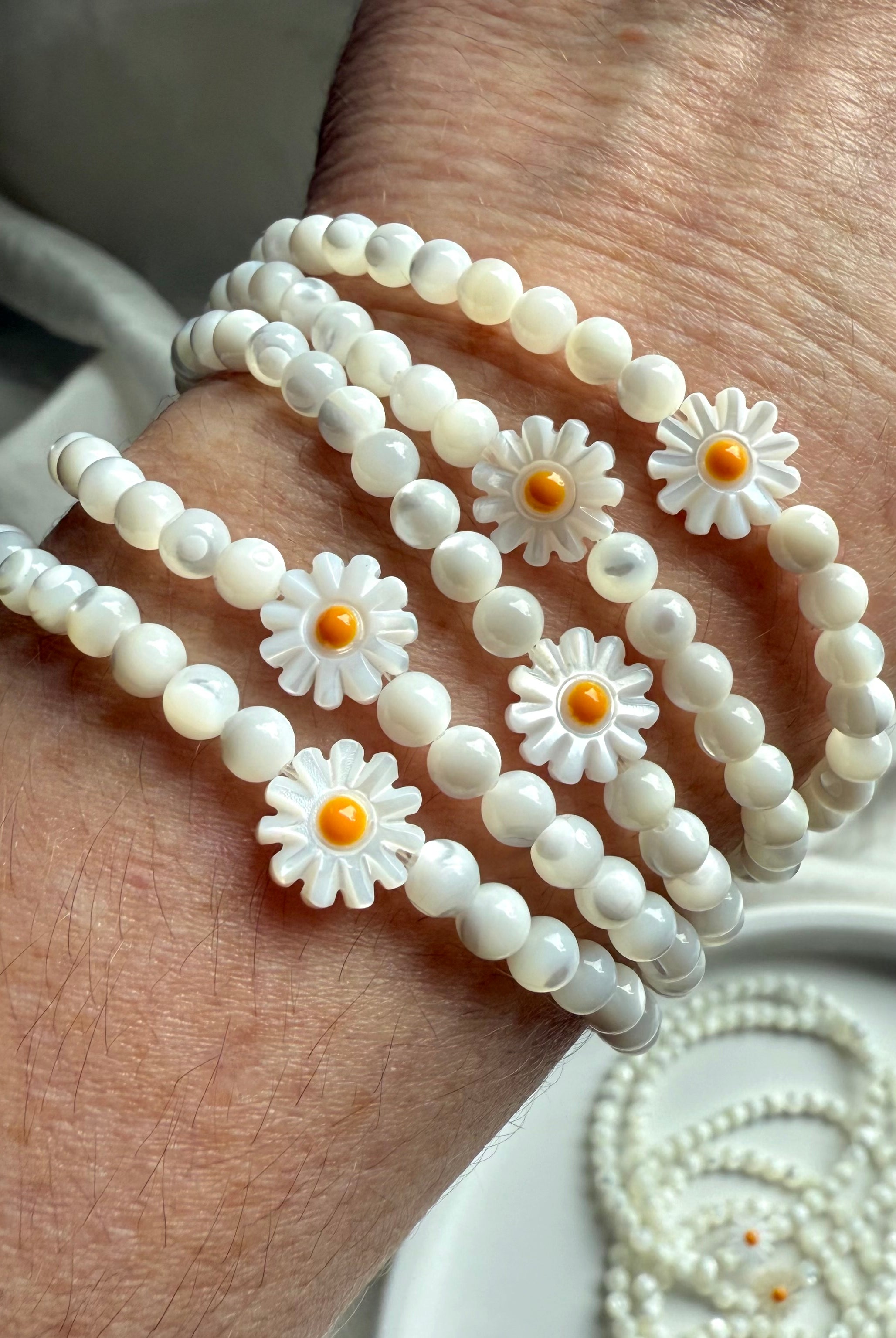 Multiple Mother of Pearl daisy bracelets stacked on wrist, glowing with soft iridescent shine – cheerful crystal jewelry gift