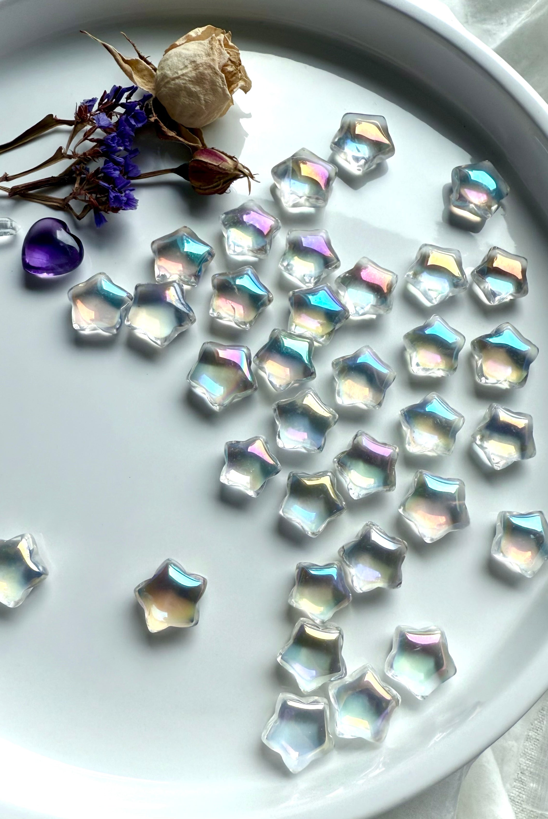 Opalescent mini aura quartz stars with rainbow sheen displayed on white tray with dried flowers, amethyst heart, and quartz points — healing crystals for universal chakra balance