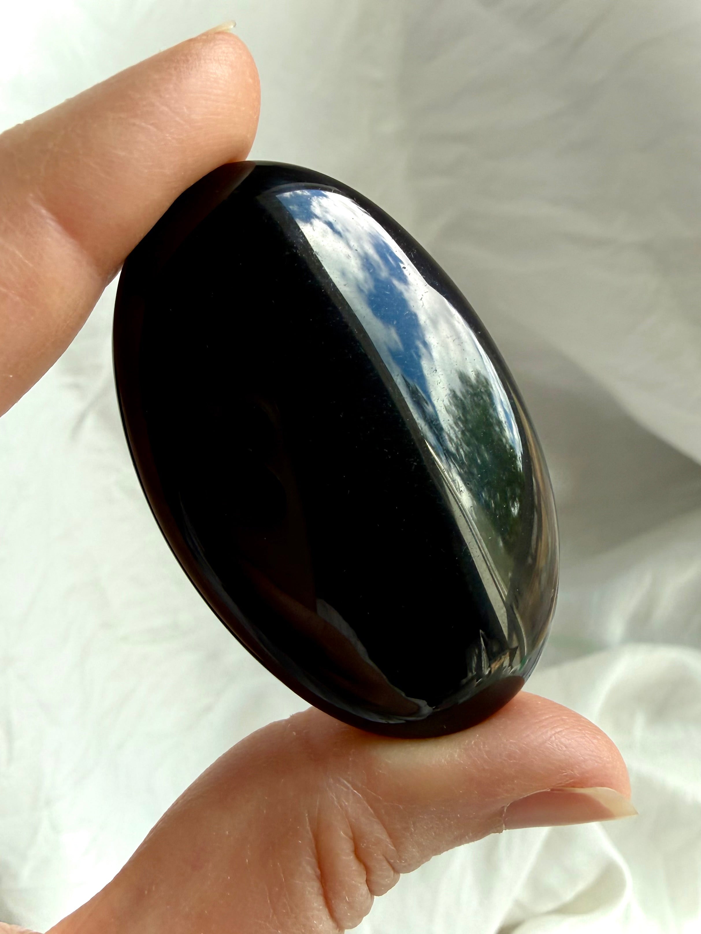 Black Obsidian palm stone held in natural light highlighting its deep black gloss and polished surface