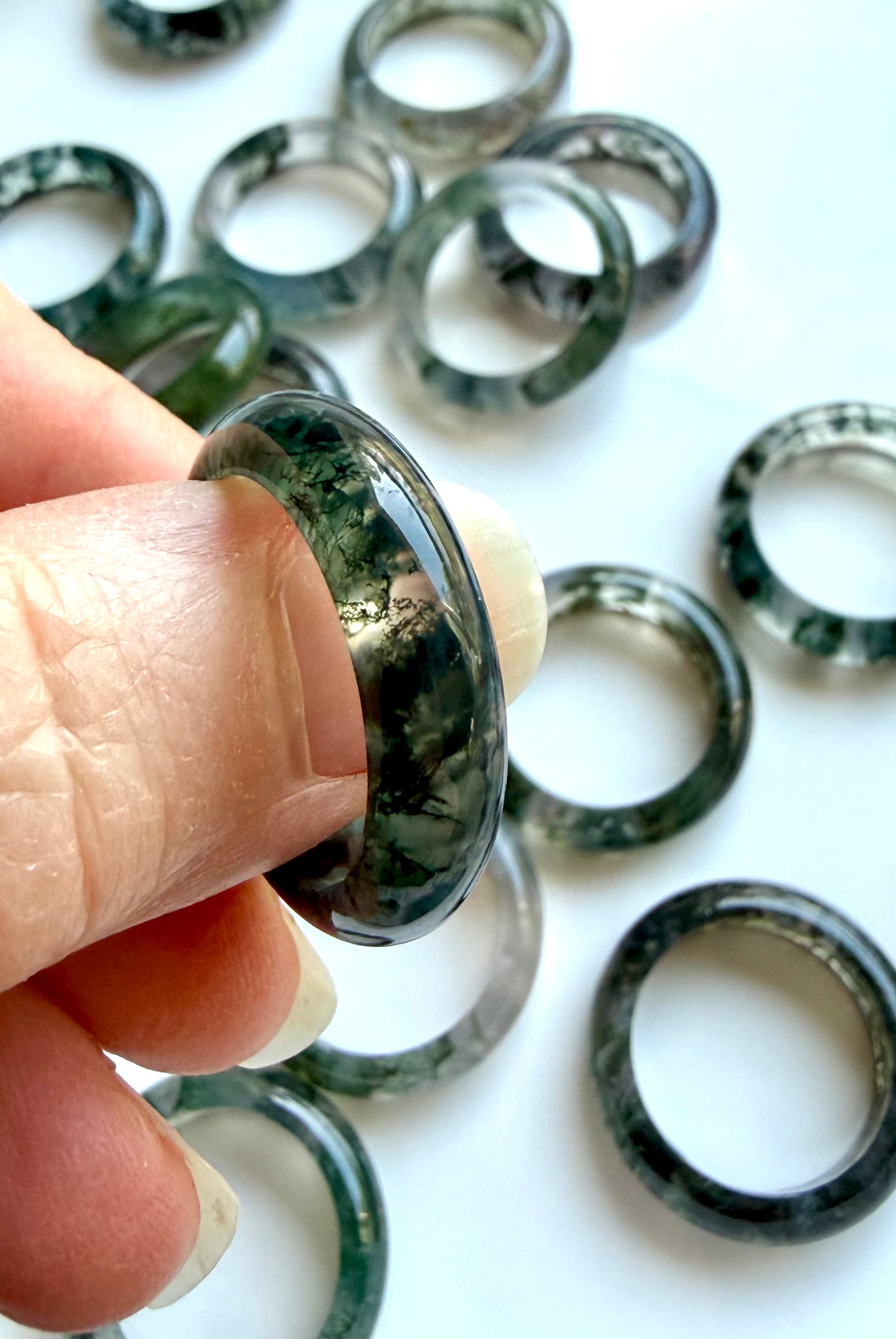 close-up moss agate ring between fingers with detailed dendritic patterning, translucent crystal for grounding clarity and renewal
