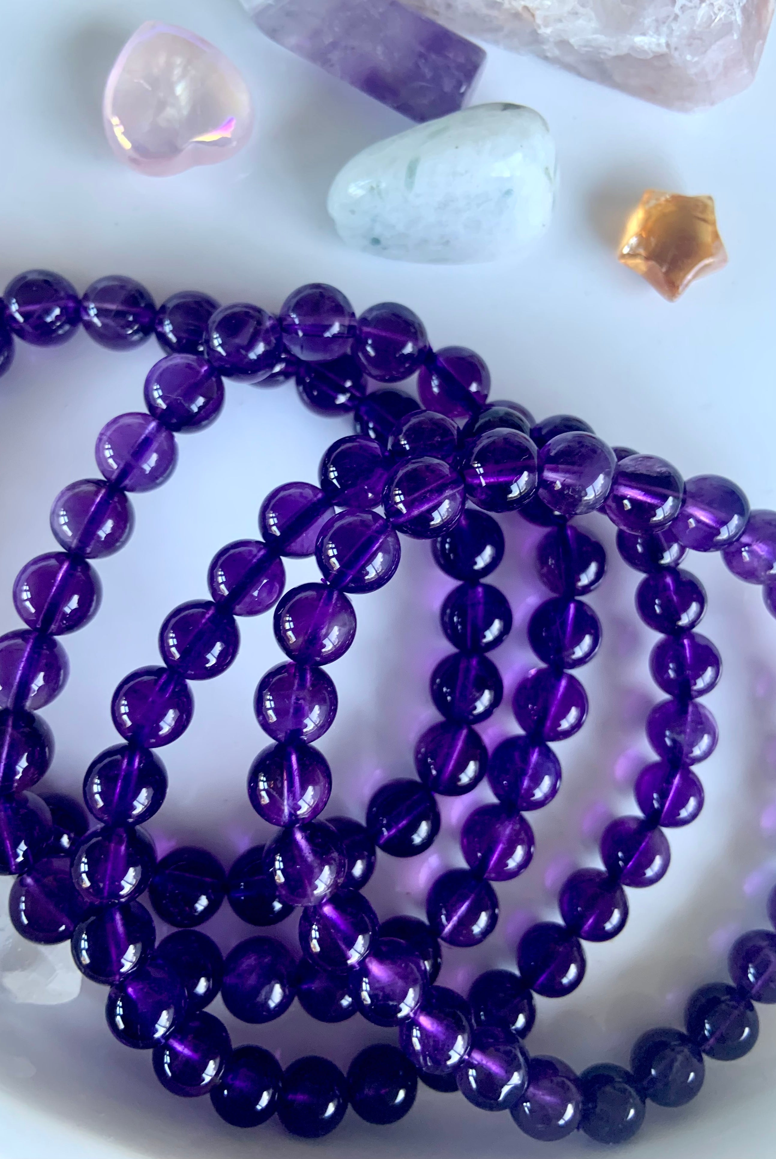 Overhead view of high quality deep purple amethyst beaded bracelets on a white plate with mini crystals in the background
