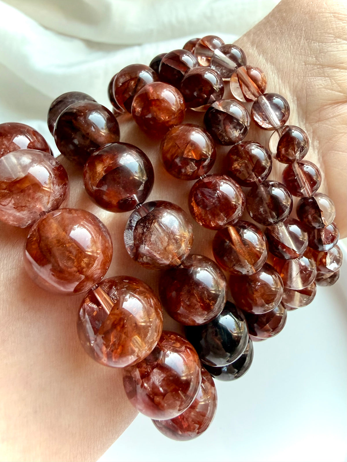 Fire Quartz bracelets stacked on a wrist, showing natural variation in deep red, burgundy and smoky Hematoid Quartz beads