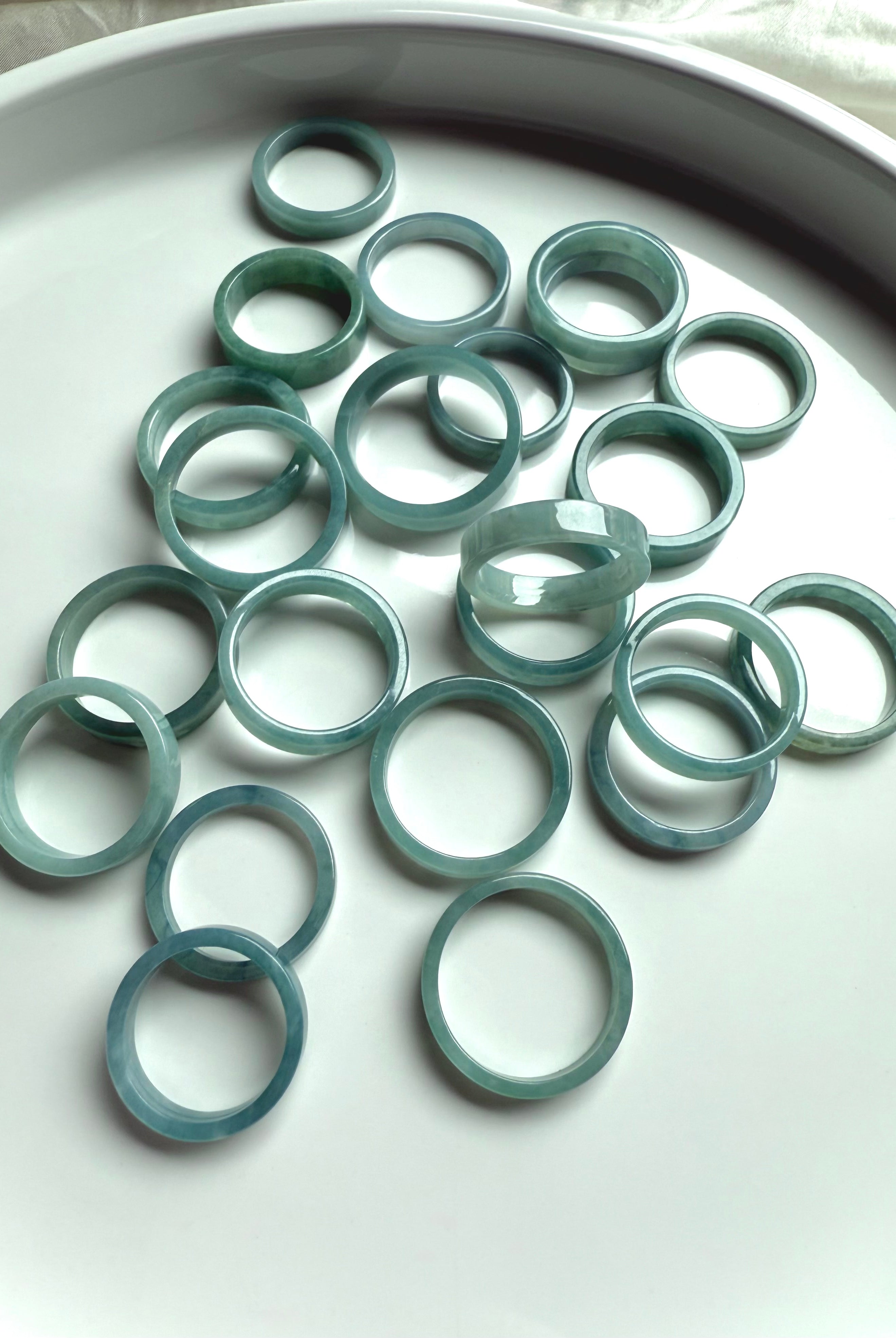 Natural jadeite rings in calming blue-green hues laid out on a white ceramic tray