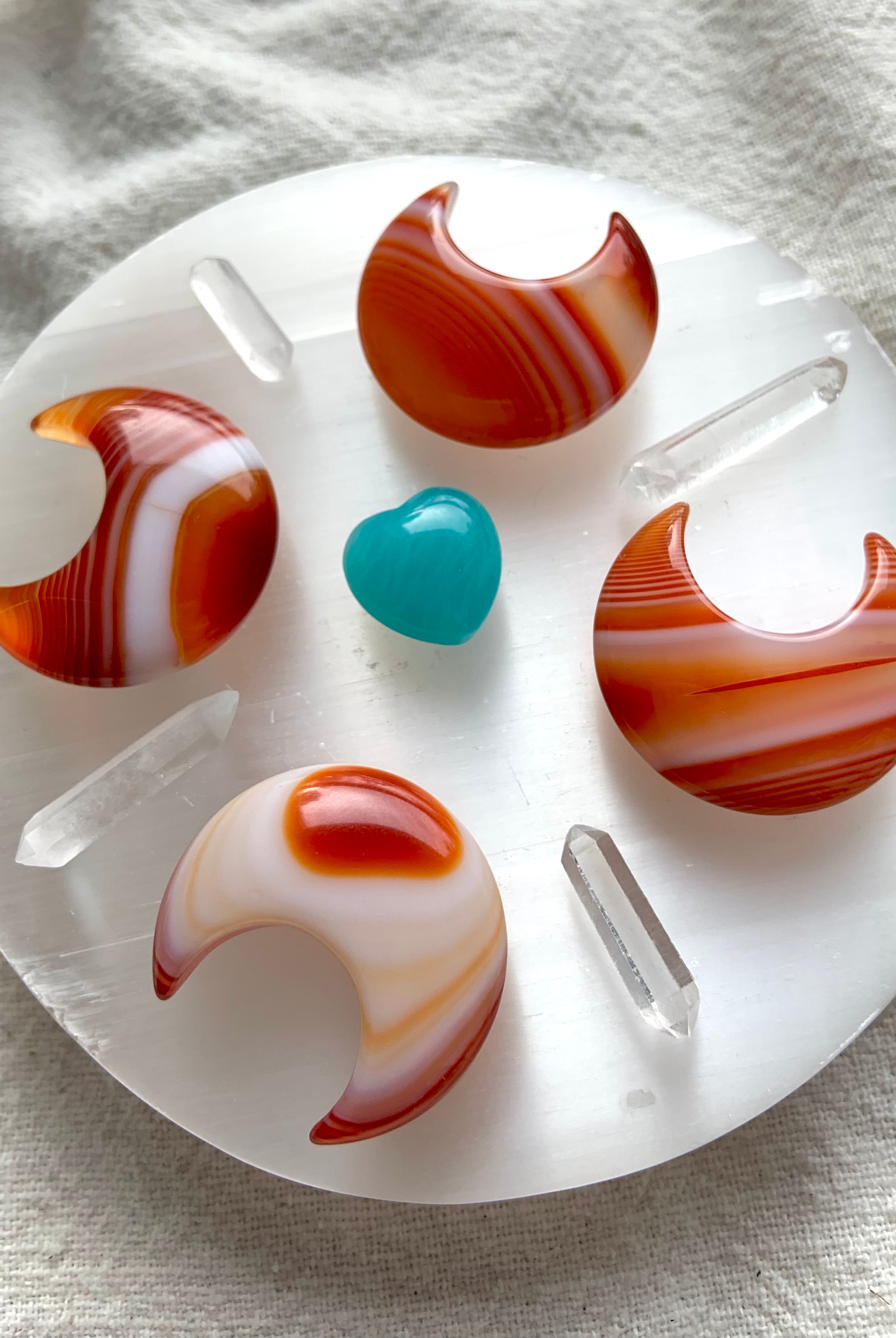 A crystal grid made from Banded Carnelian Moons, clear quartz points and an amazonite heart in the center on top of a selenite plate