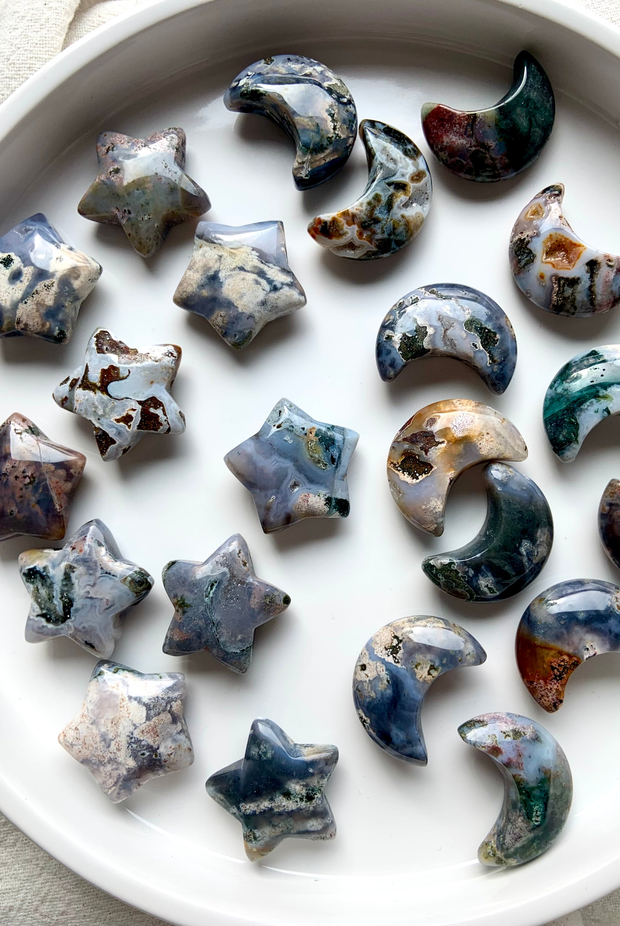 Array of Cosmic Ocean Jasper moons and stars carvings on round white dish, colorful celestial crystals for altar décor and crystal healing