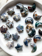 Array of Cosmic Ocean Jasper moons and stars carvings on round white dish, colorful celestial crystals for altar décor and crystal healing