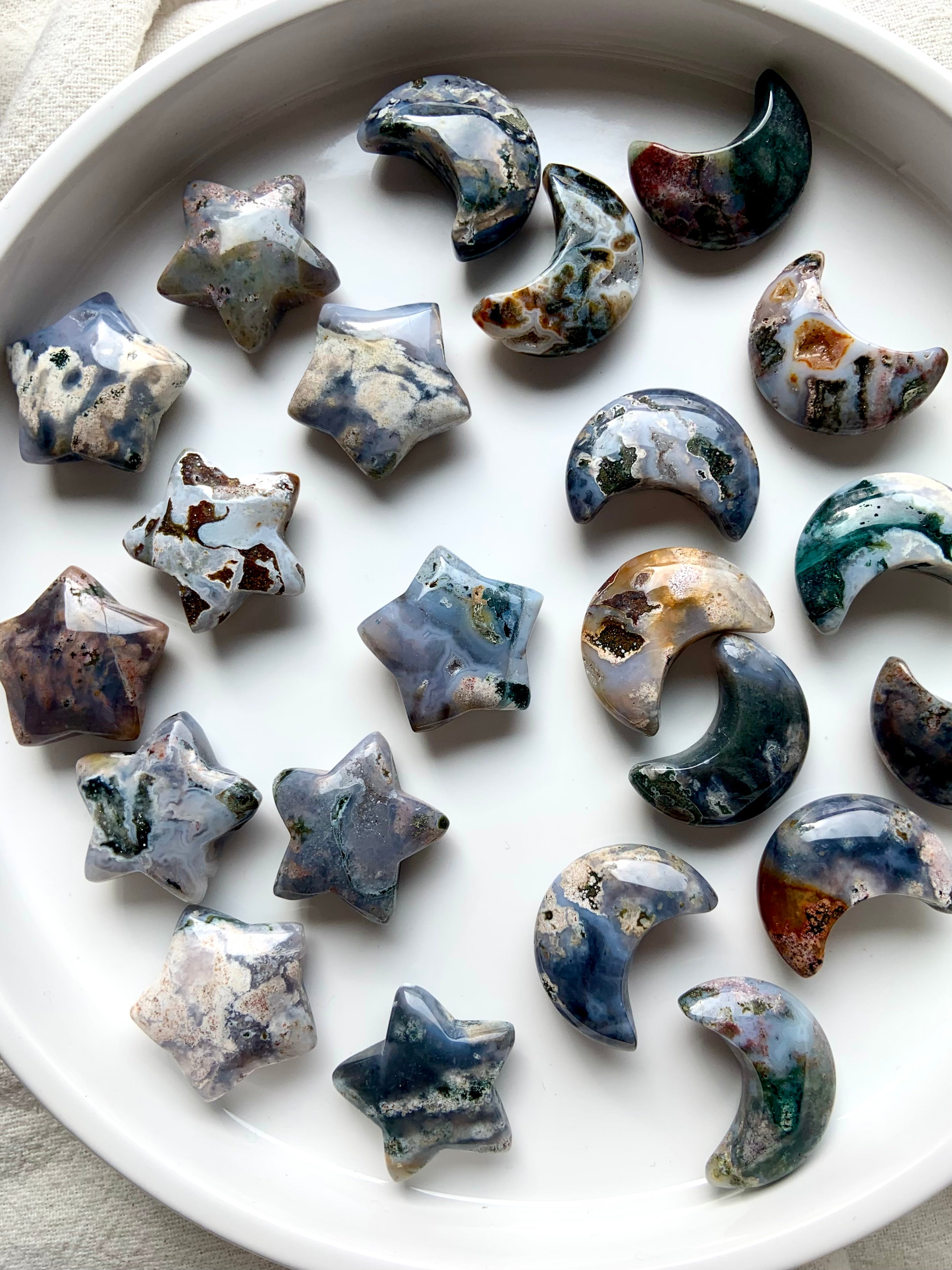 Array of Cosmic Ocean Jasper moons and stars carvings on round white dish, colorful celestial crystals for altar décor and crystal healing