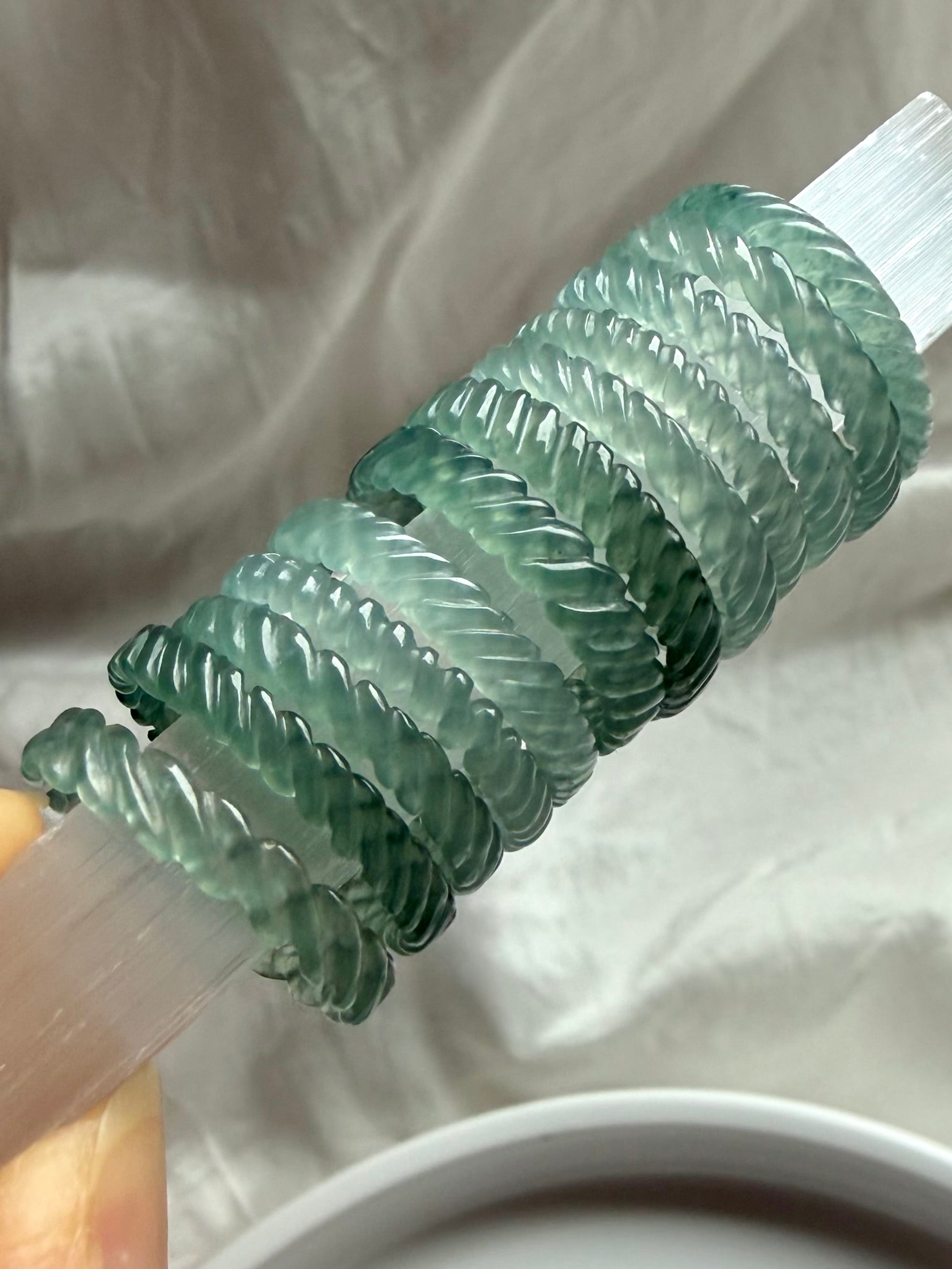Collector-quality Guatemalan Blue Water Jade woven rings stacked on selenite, showcasing braided carving and glowing translucency