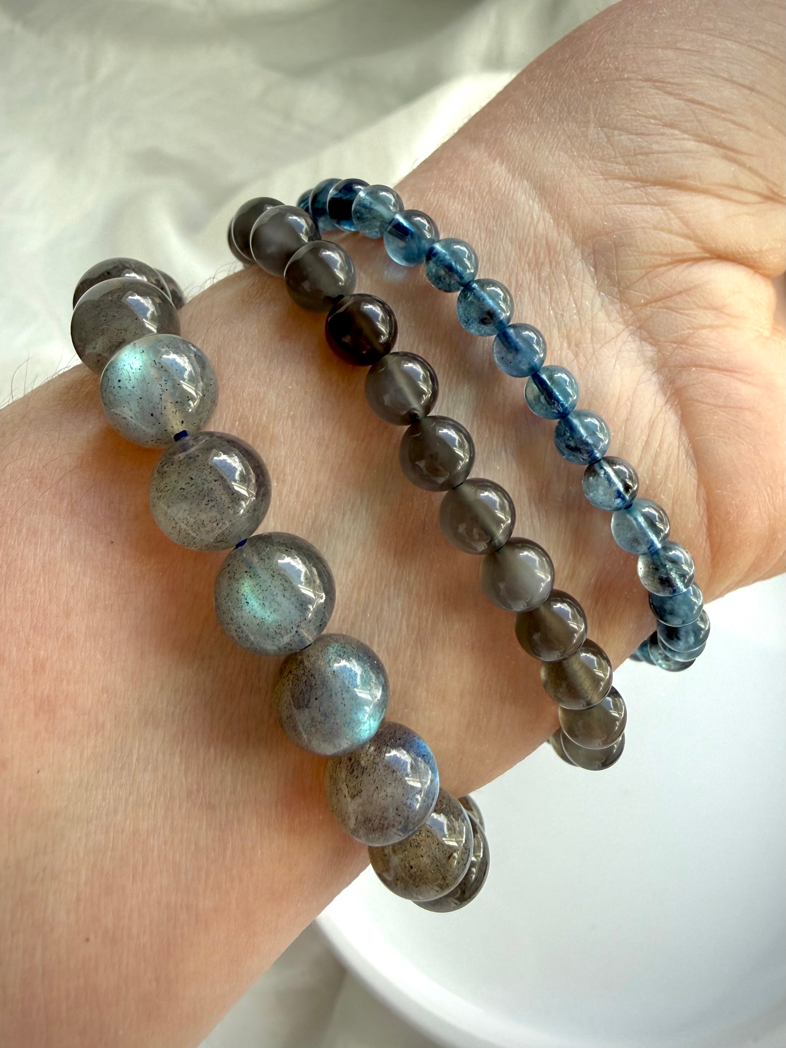 Labradorite, Black Moonstone, and Aquamarine crystal bracelets stacked together on wrist for layering inspiration