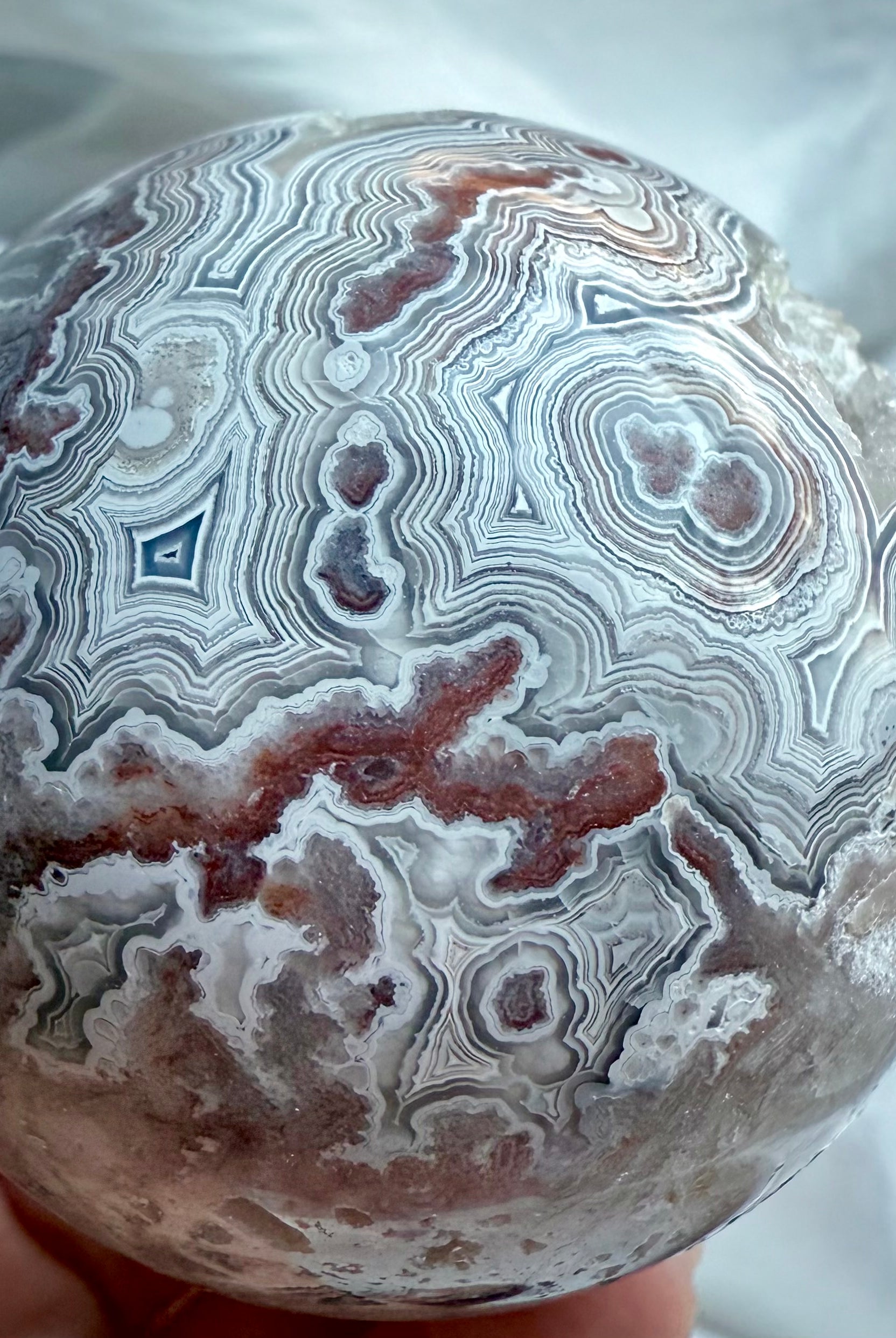 Close-up of high-grade Crazy Lace Agate sphere featuring geometric lace banding, crystal druzy pocket, and rich red tones
