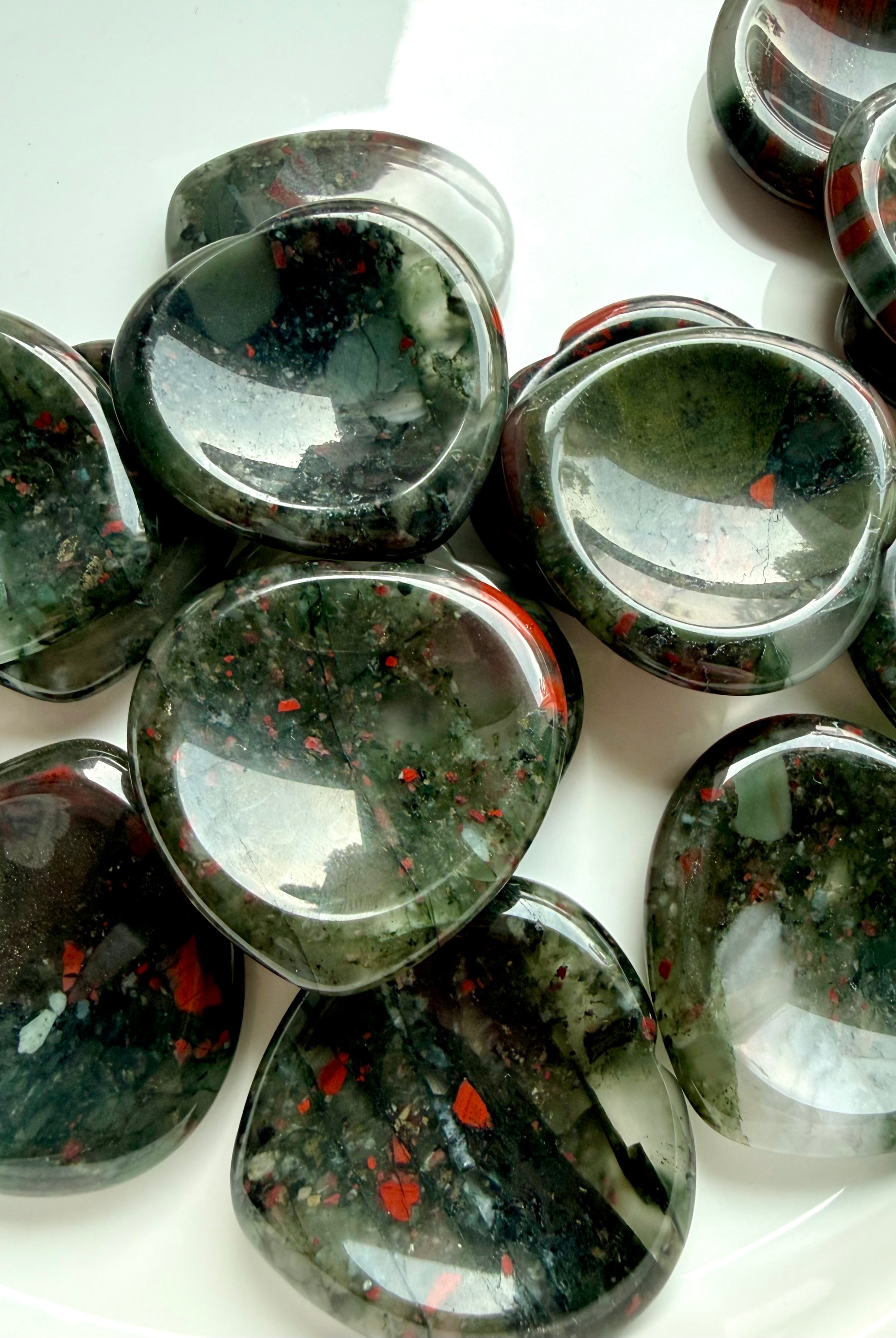 group of bloodstone heart worry stones scattered on white surface, polished crystals for grounding emotional support and balance
