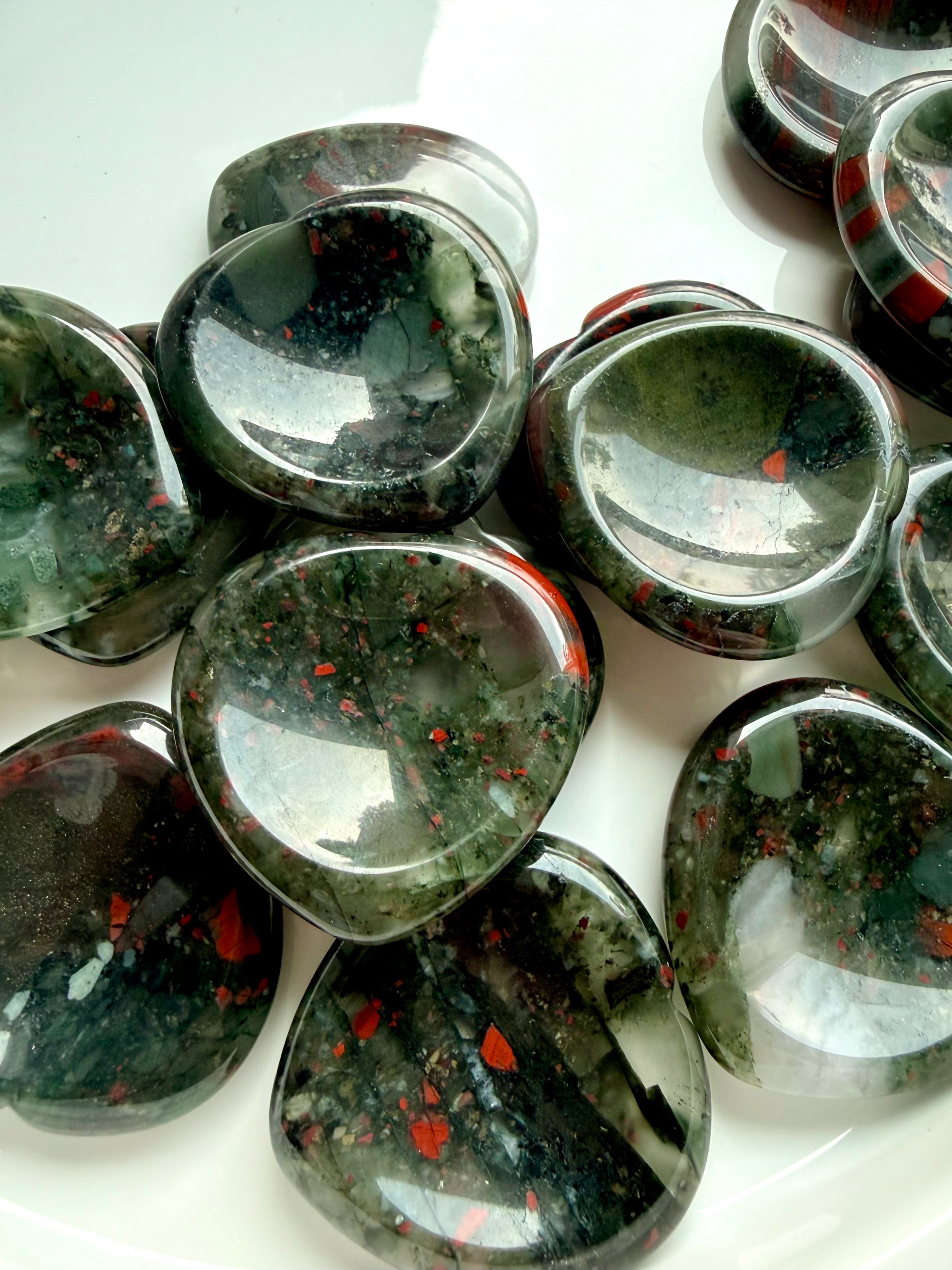 group of bloodstone heart worry stones scattered on white surface, polished crystals for grounding emotional support and balance