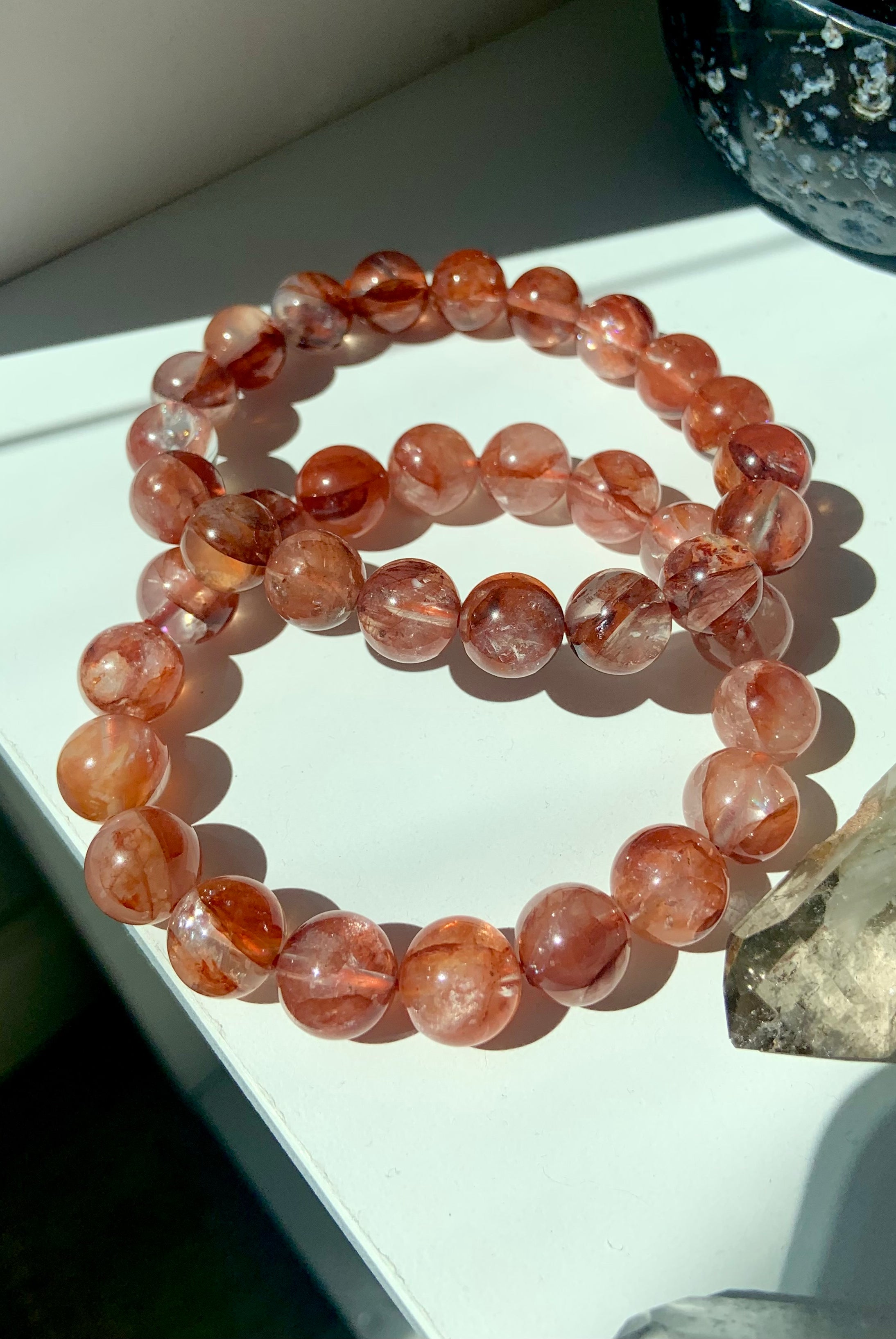 Lifestyle image of two Fire Quartz bracelets on a white surface with smoky quartz points, healing crystals for Root Chakra energy