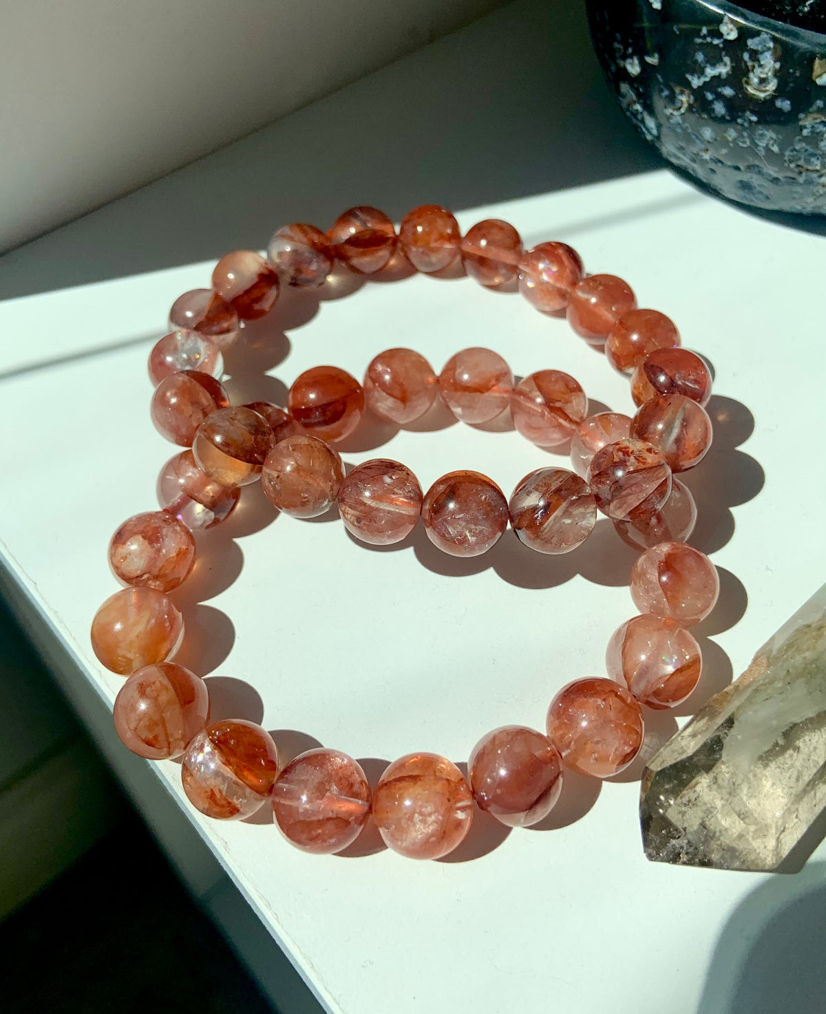 Lifestyle image of two Fire Quartz bracelets on a white surface with smoky quartz points, healing crystals for Root Chakra energy