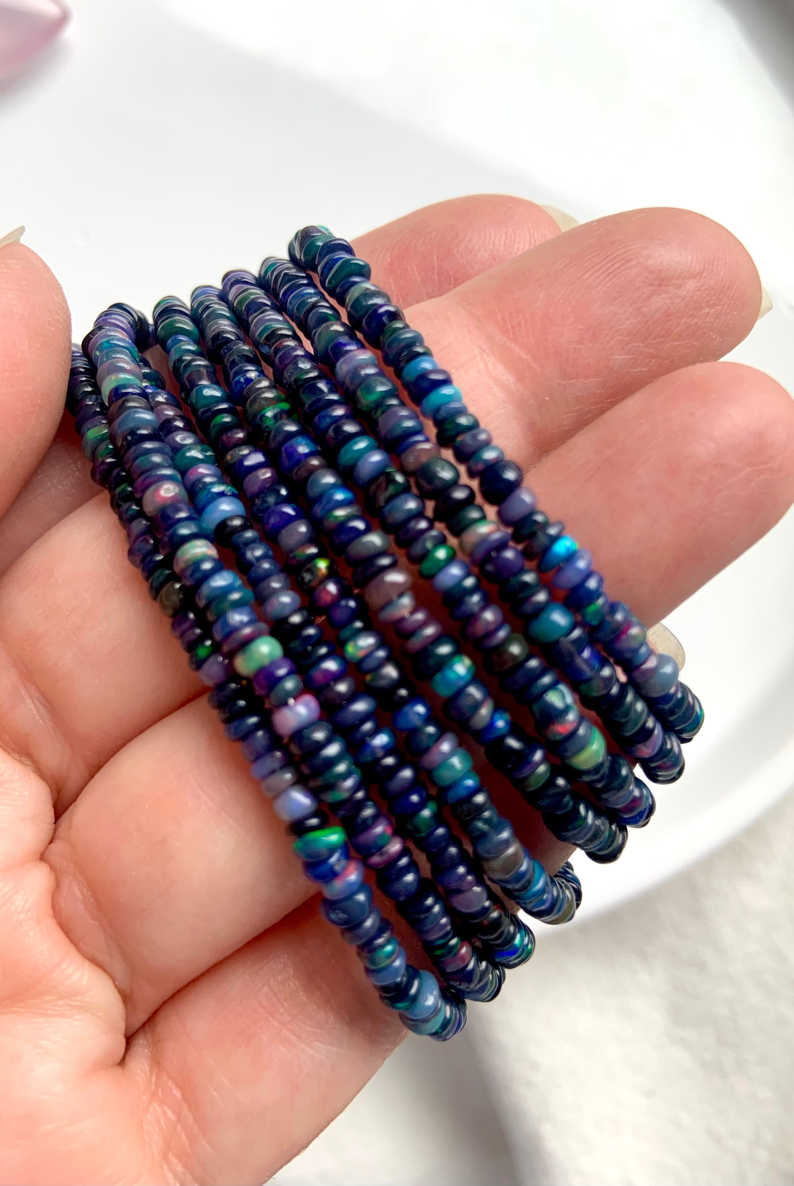 Black Fire Opal bracelets in various bead sizes held at an angle to show blue and rainbow iridescence — sterling silver clasp jewelry.