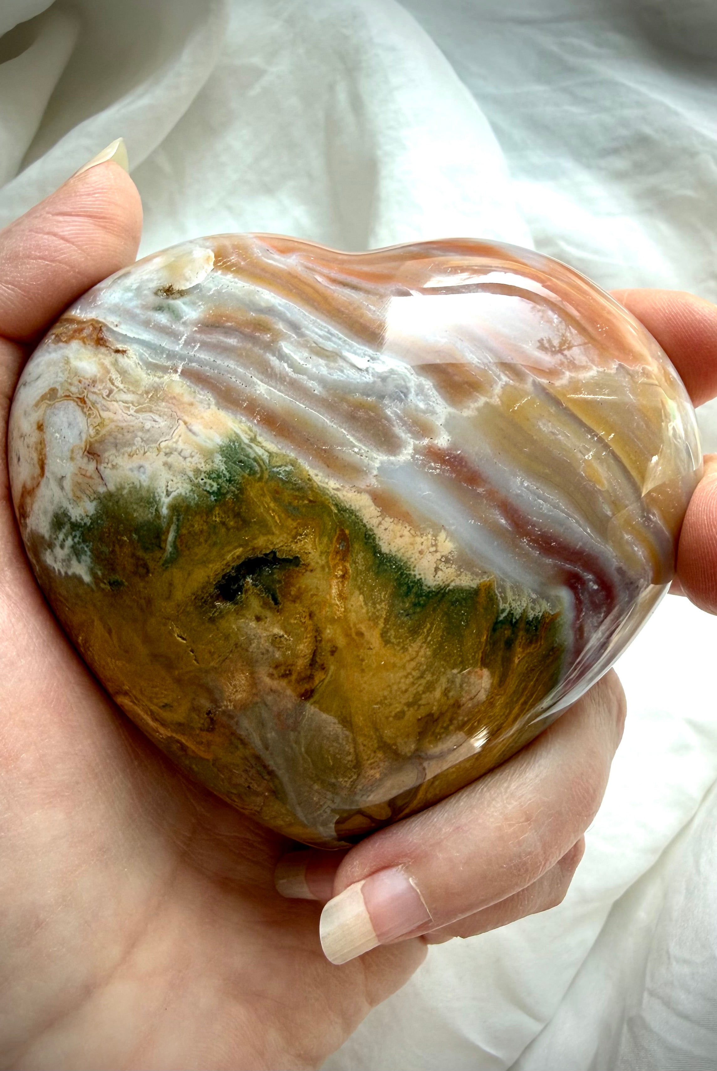 One of a kind Ocean Jasper heart crystal also known as sea jasper, with flowing agate banding in caramel, cream, moss green and soft grey tones, held in hand