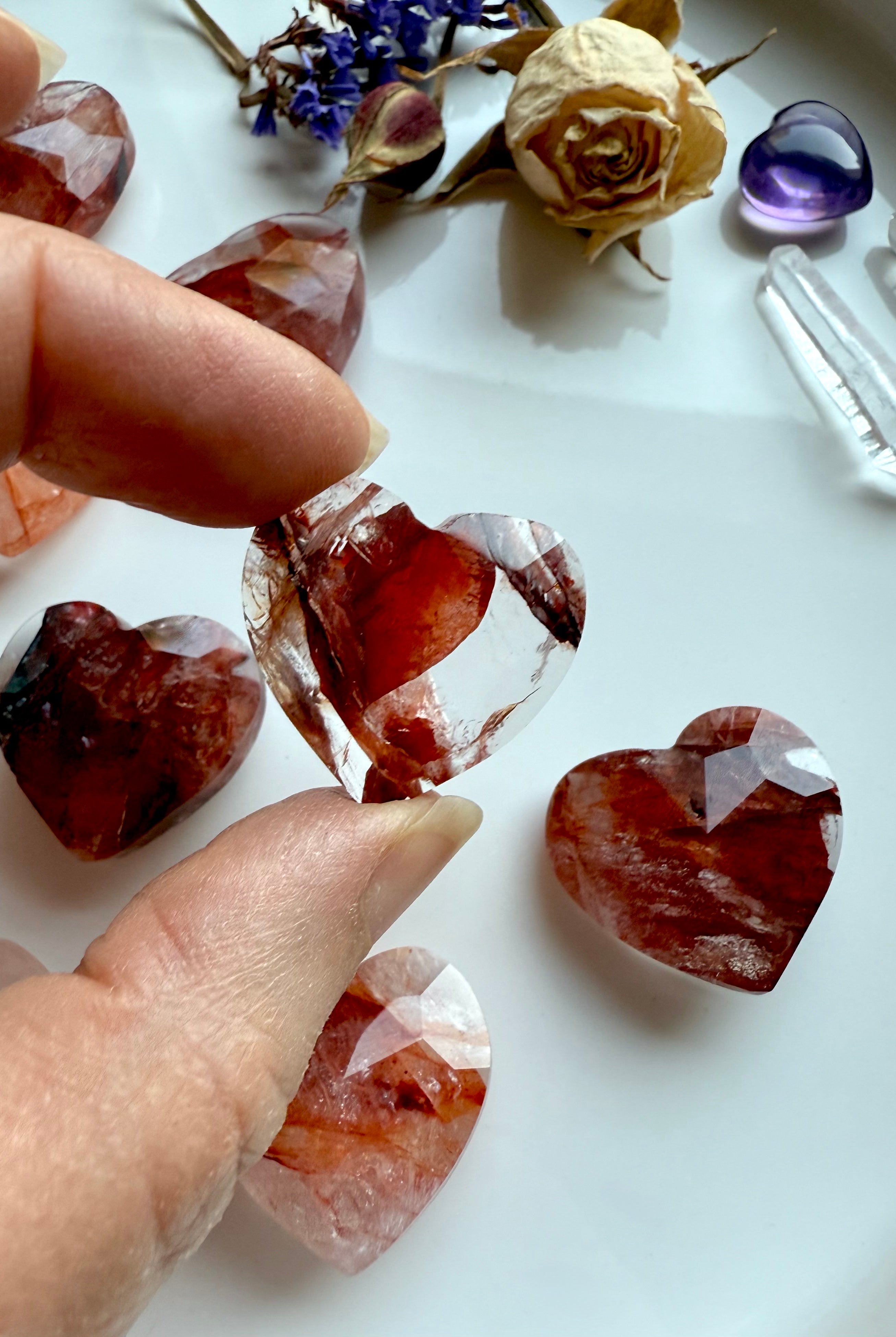 Close-up of faceted Fire Quartz heart crystal with more in the background – mini hematoid quartz hearts for grounding and energy healing