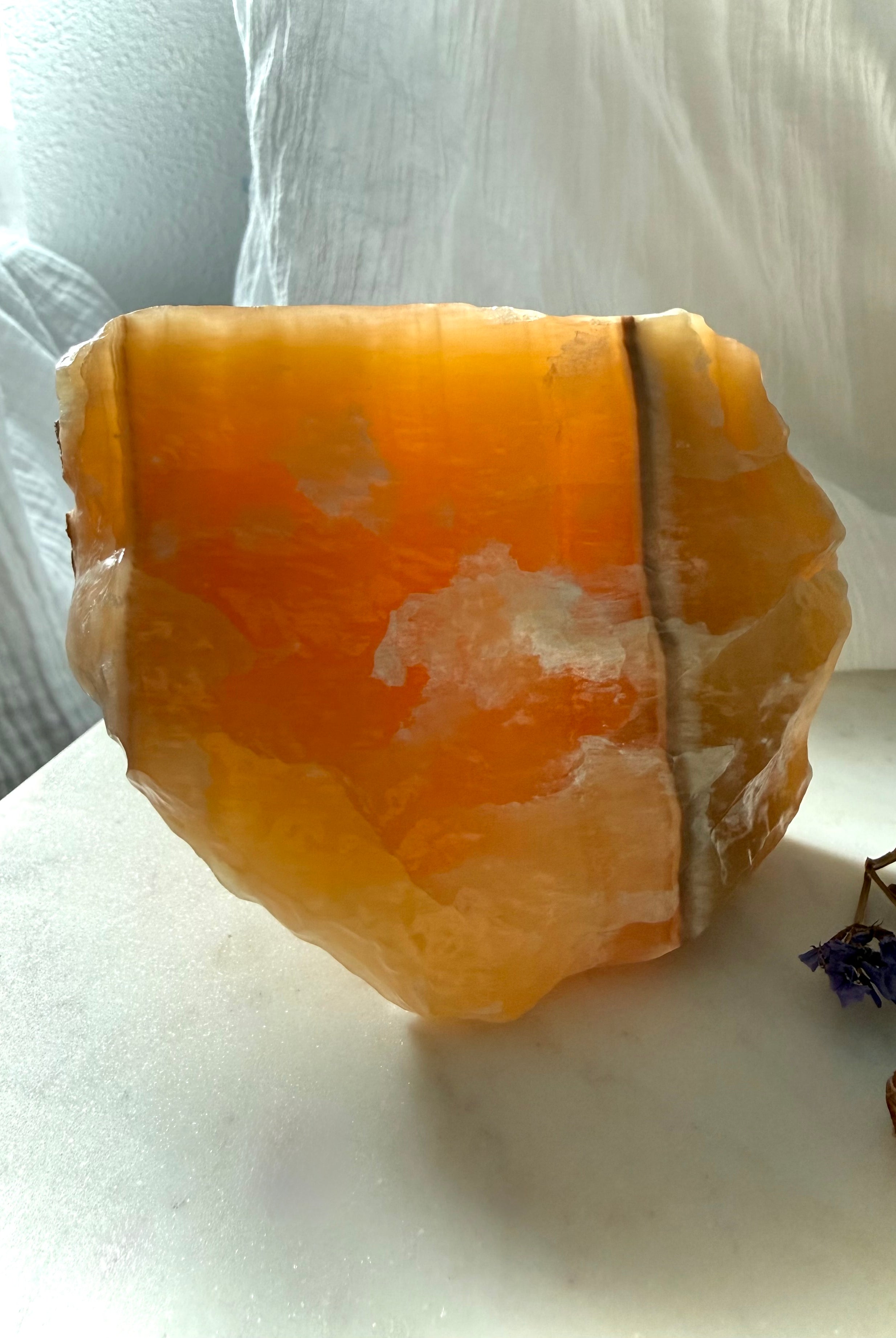 Translucent Orange Calcite display specimen illuminated by natural light with glowing orange interior and mineral banding