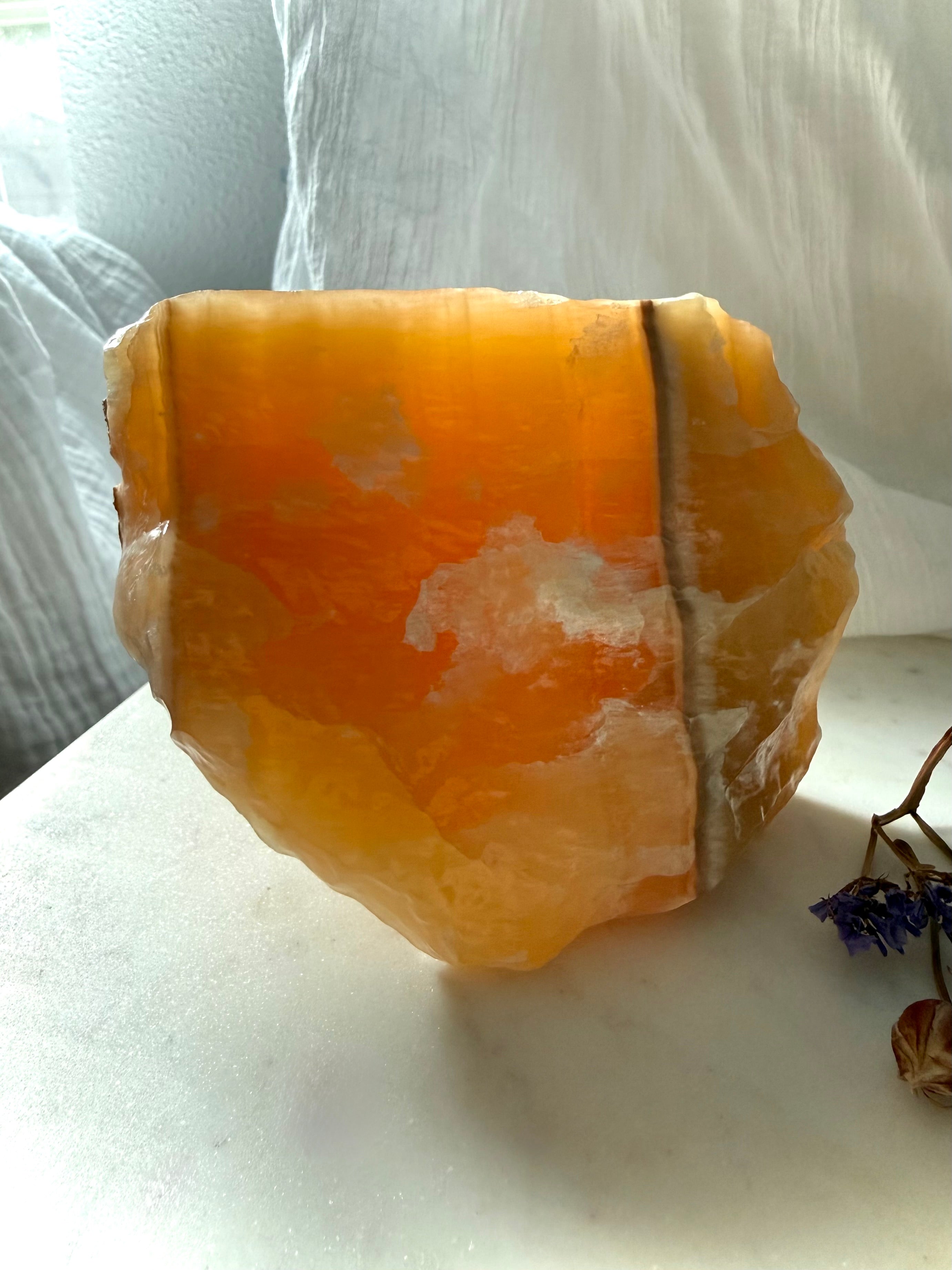 Translucent Orange Calcite display specimen illuminated by natural light with glowing orange interior and mineral banding