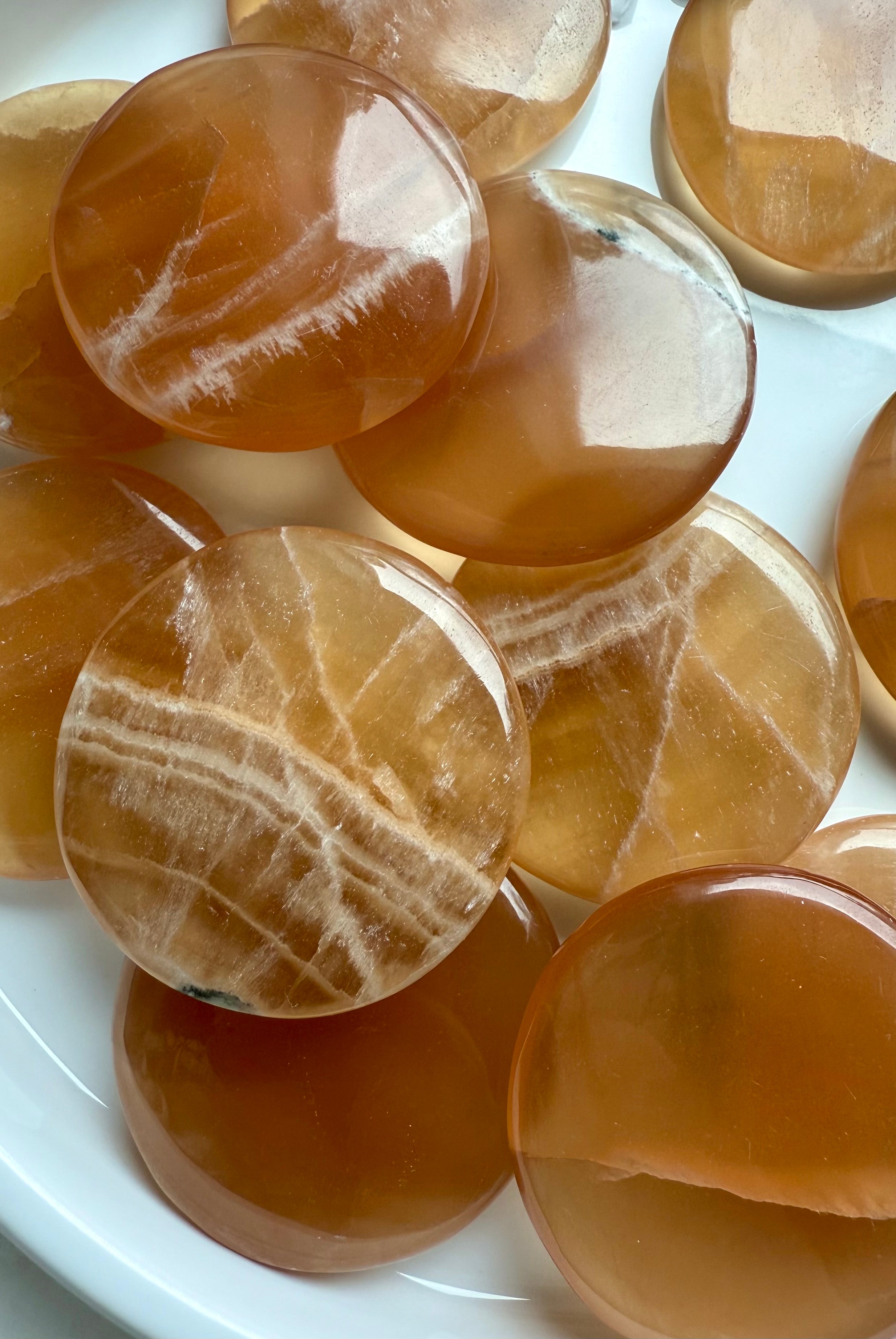 Close-up of polished Honey Calcite palm stones with banded patterns, glowing with warm amber tones for confidence, focus, and gentle empowerment.