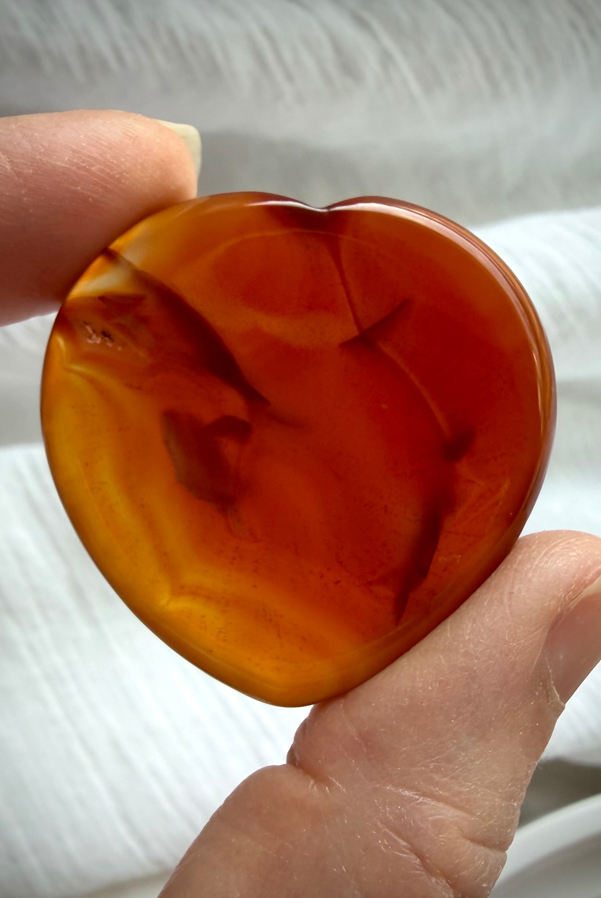 Translucent Carnelian heart worry stone with amber-orange color, darker natural inclusions and glossy polish