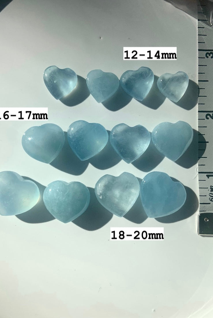 Aquamarine crystal hearts in 3 rows by size with measuring tape — mini hearts sized 12–14mm, 16–17mm, 18–20mm for throat chakra crystal healing.