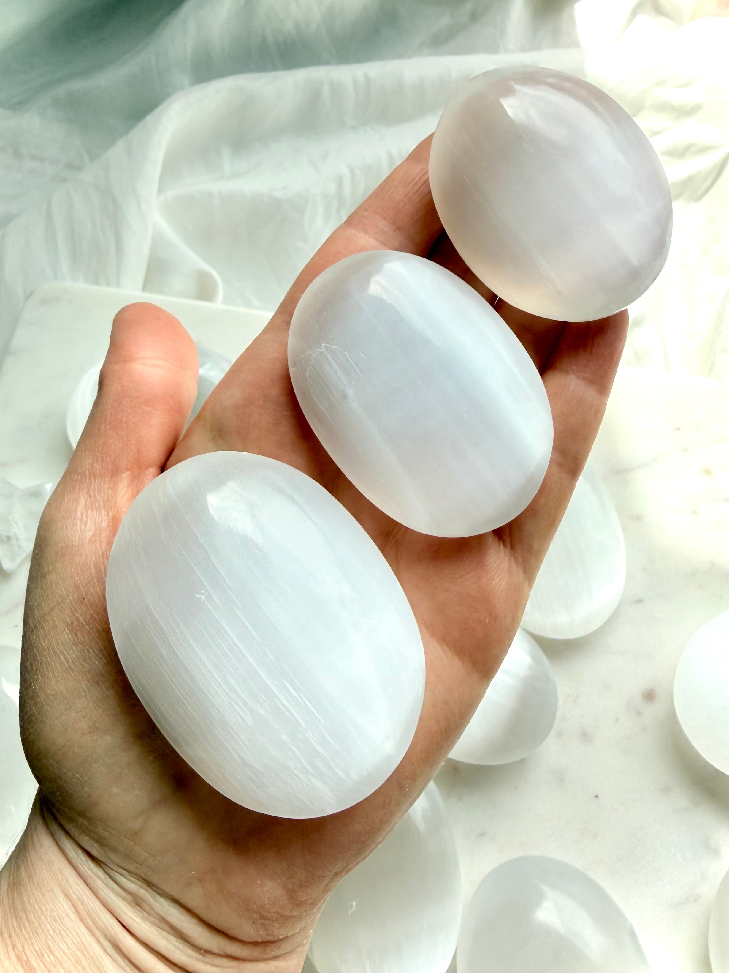 Selenite palm stones in natural light with luminous silky sheen and polished satin spar crystal for cleansing, peace, and meditation