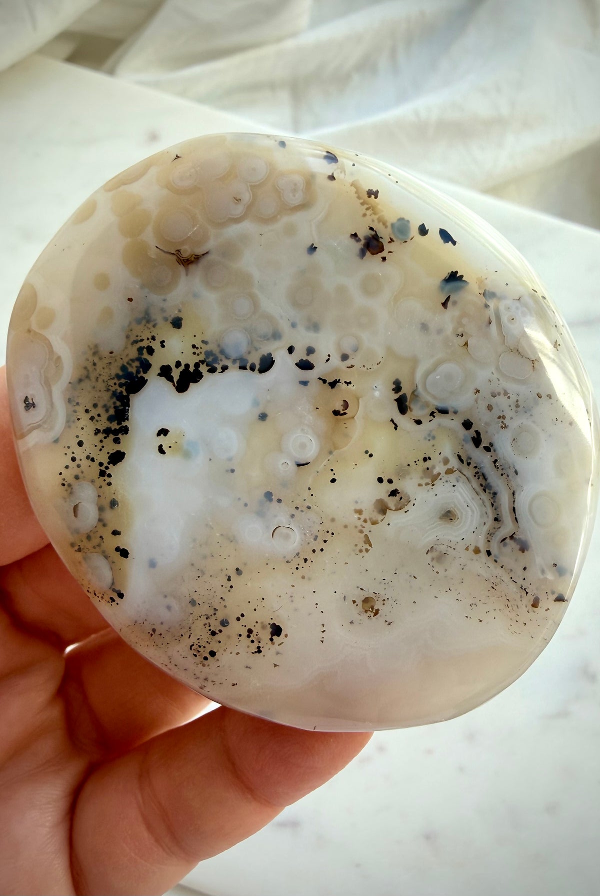 Dendritic Agate crystal held in hand, revealing earthy golden inclusions, black dendritic patterns and polished contours